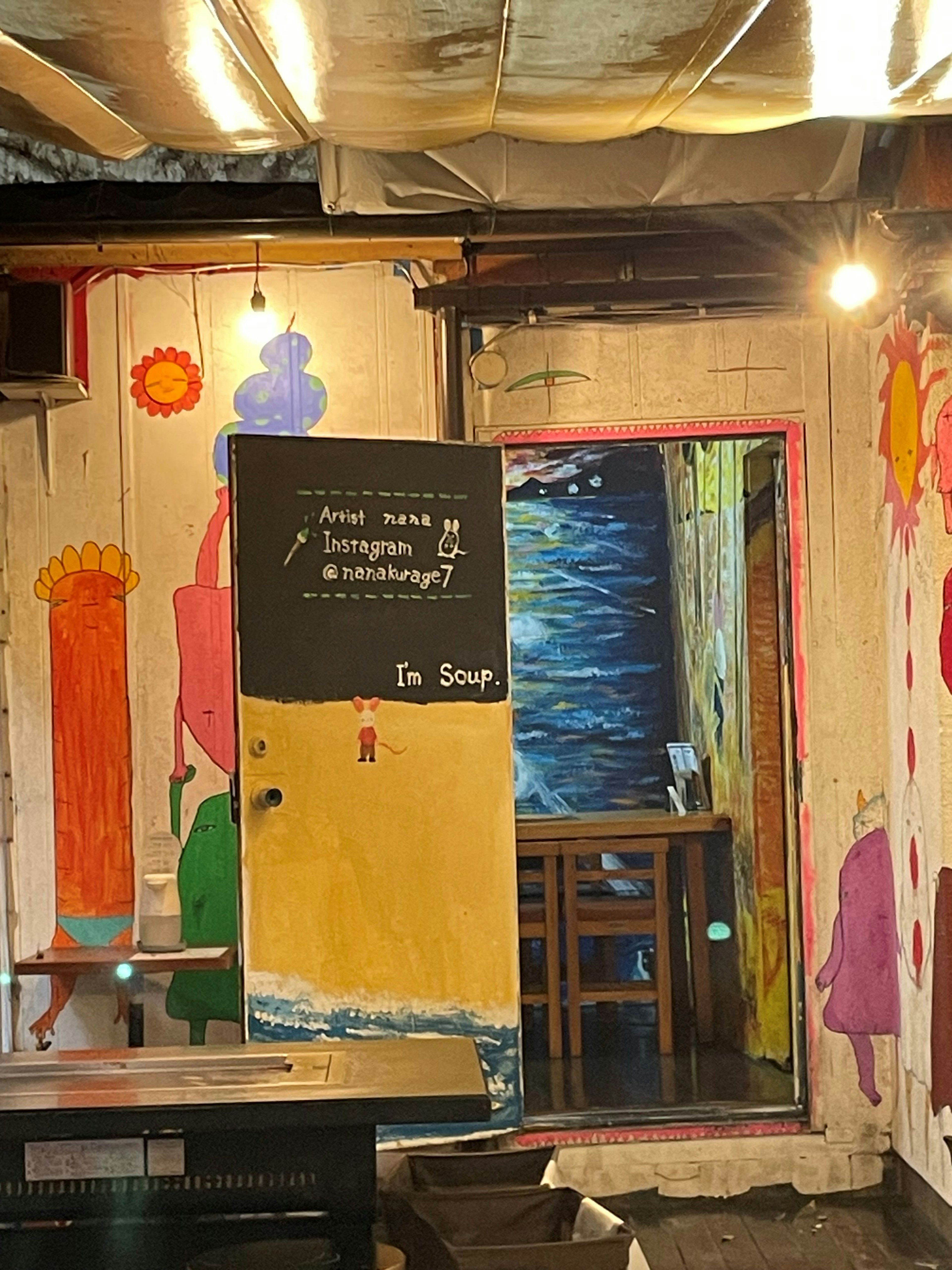 Interior de un café colorido con paredes pintadas y una puerta que conduce a una zona de comedor