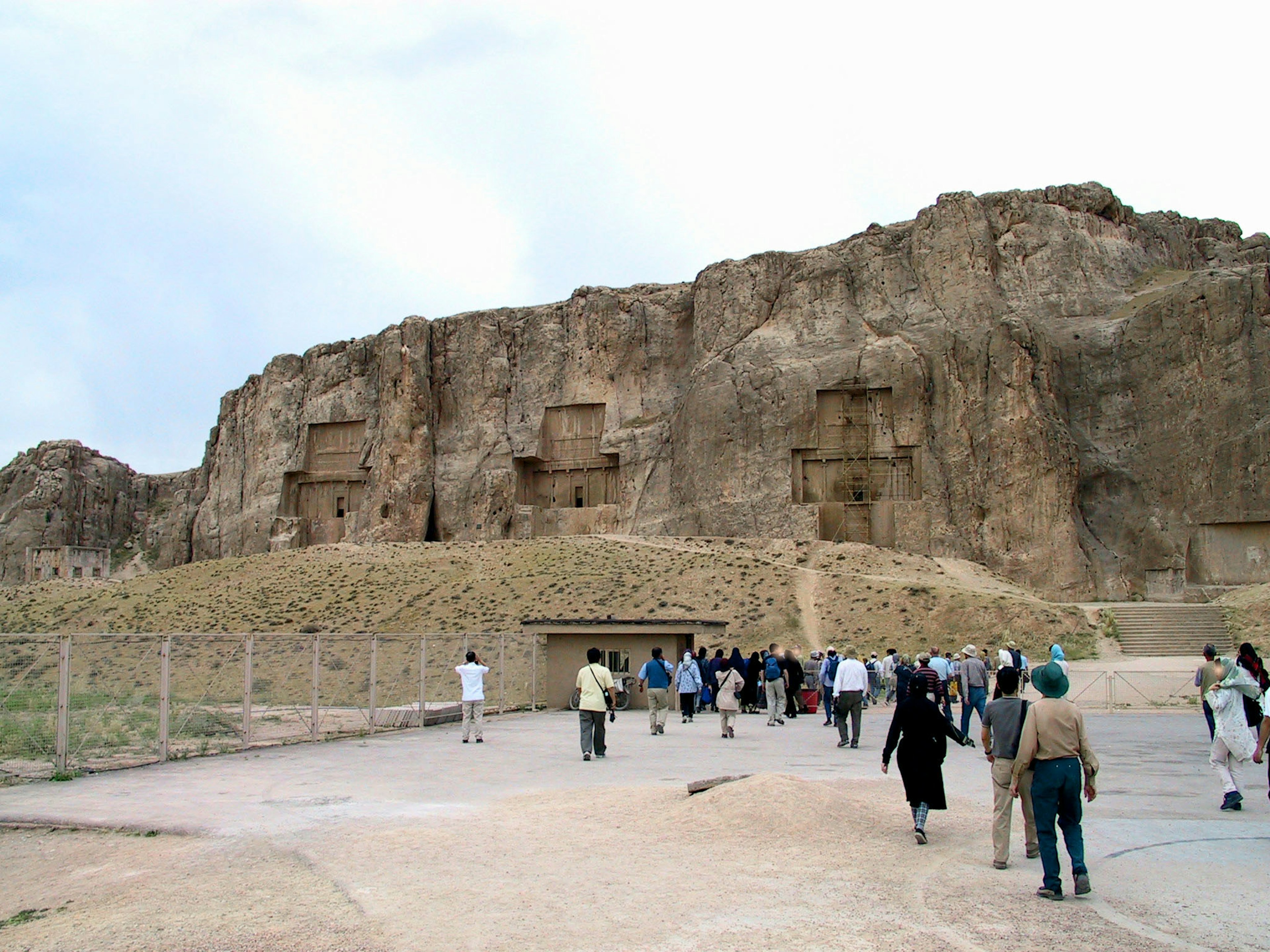 Ancient tombs carved into a rocky cliff with a group of tourists