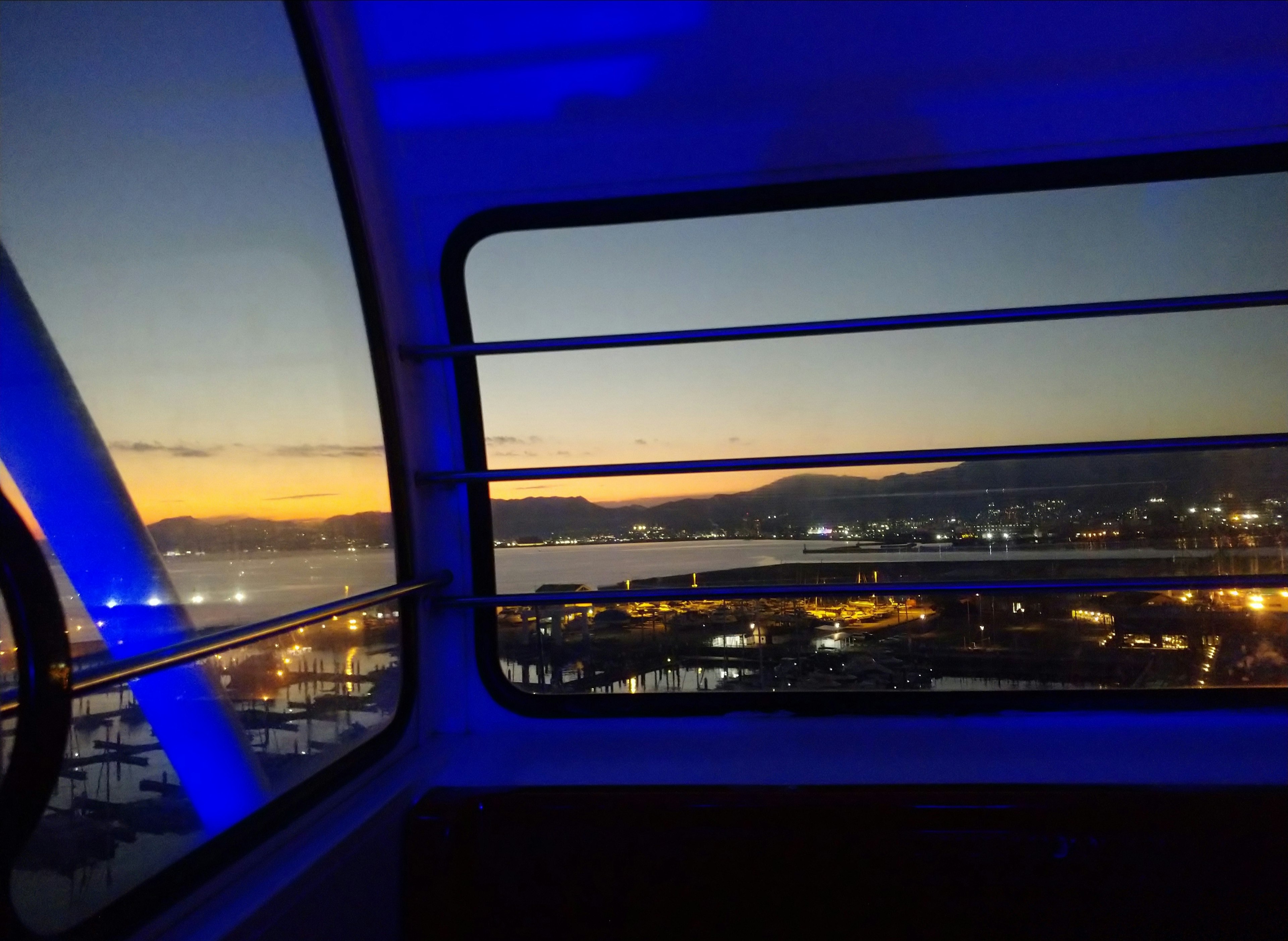 View from a Ferris wheel capsule at dusk showcasing the harbor and blue lighting