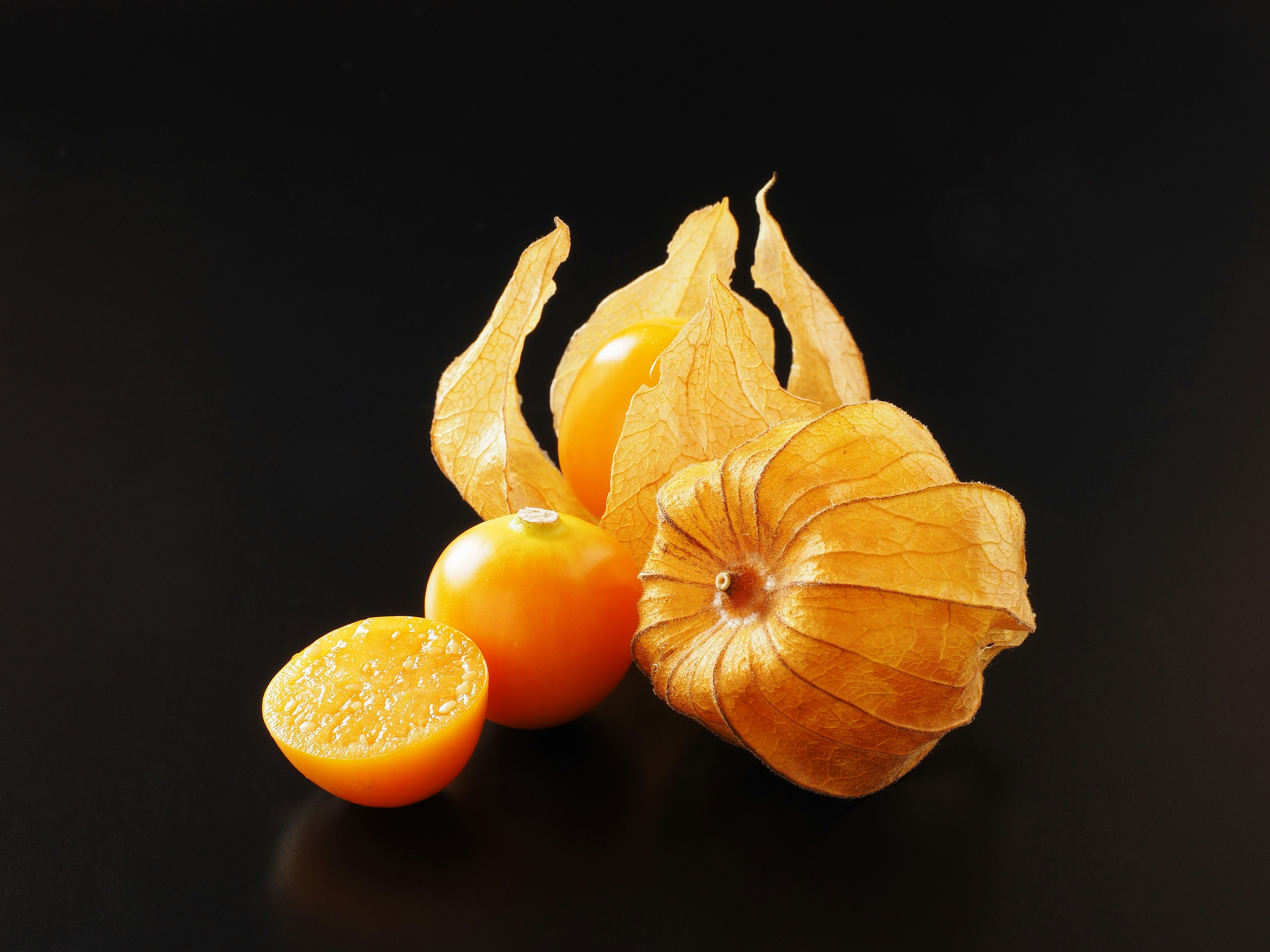 Yellow husked fruits with a cut half on a black background