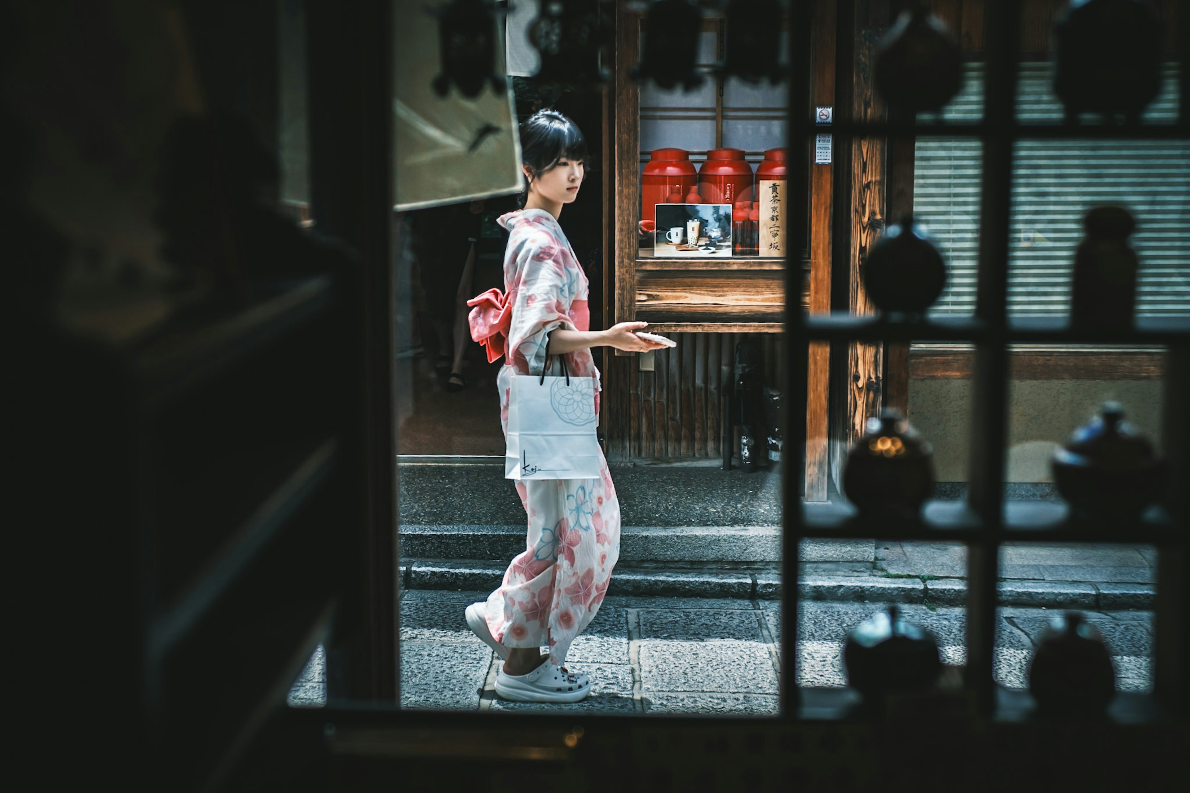 Una donna in kimono che cammina per strada vista attraverso una finestra