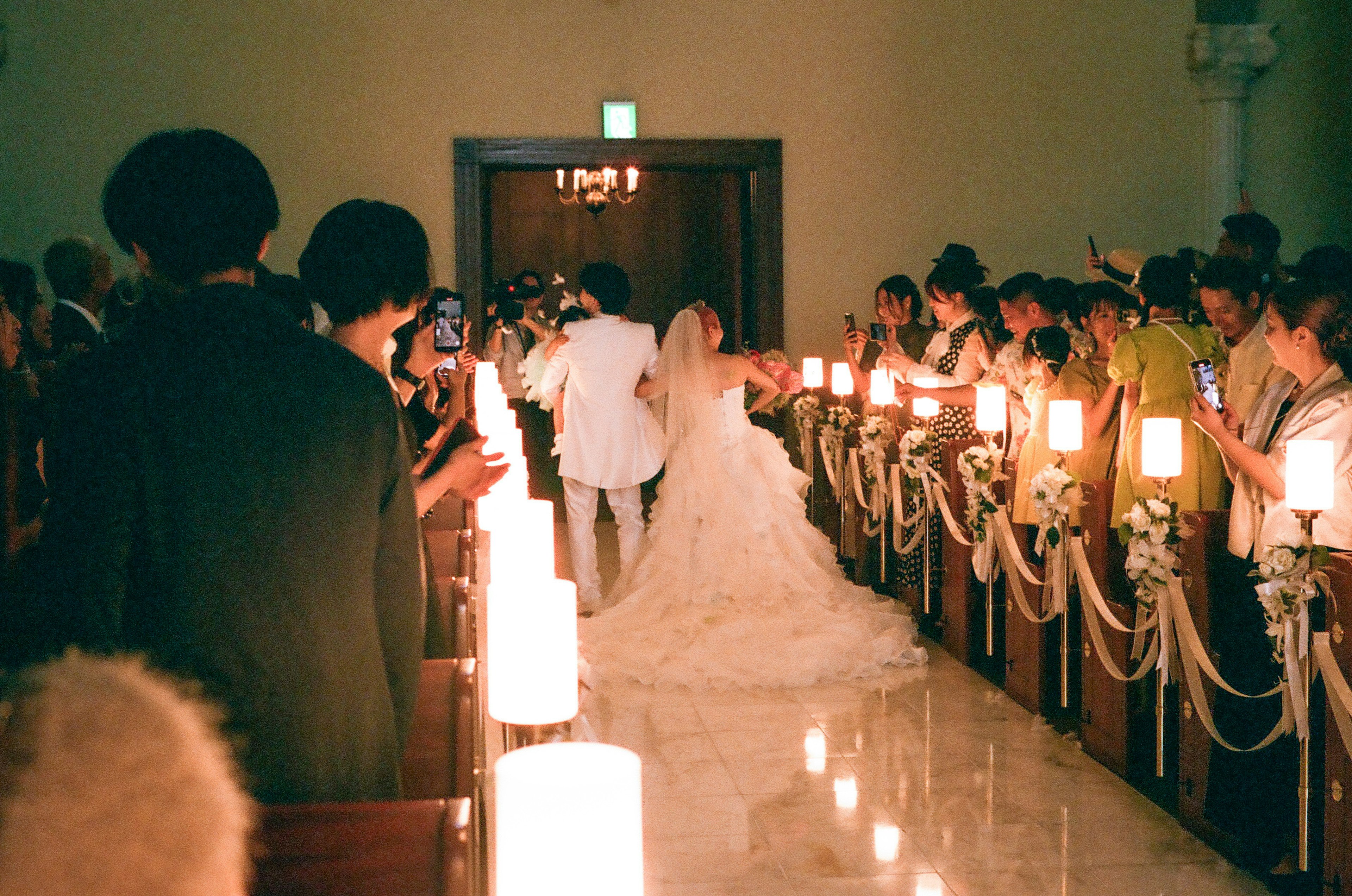 Bride and groom walking down the aisle surrounded by guests with lit candles