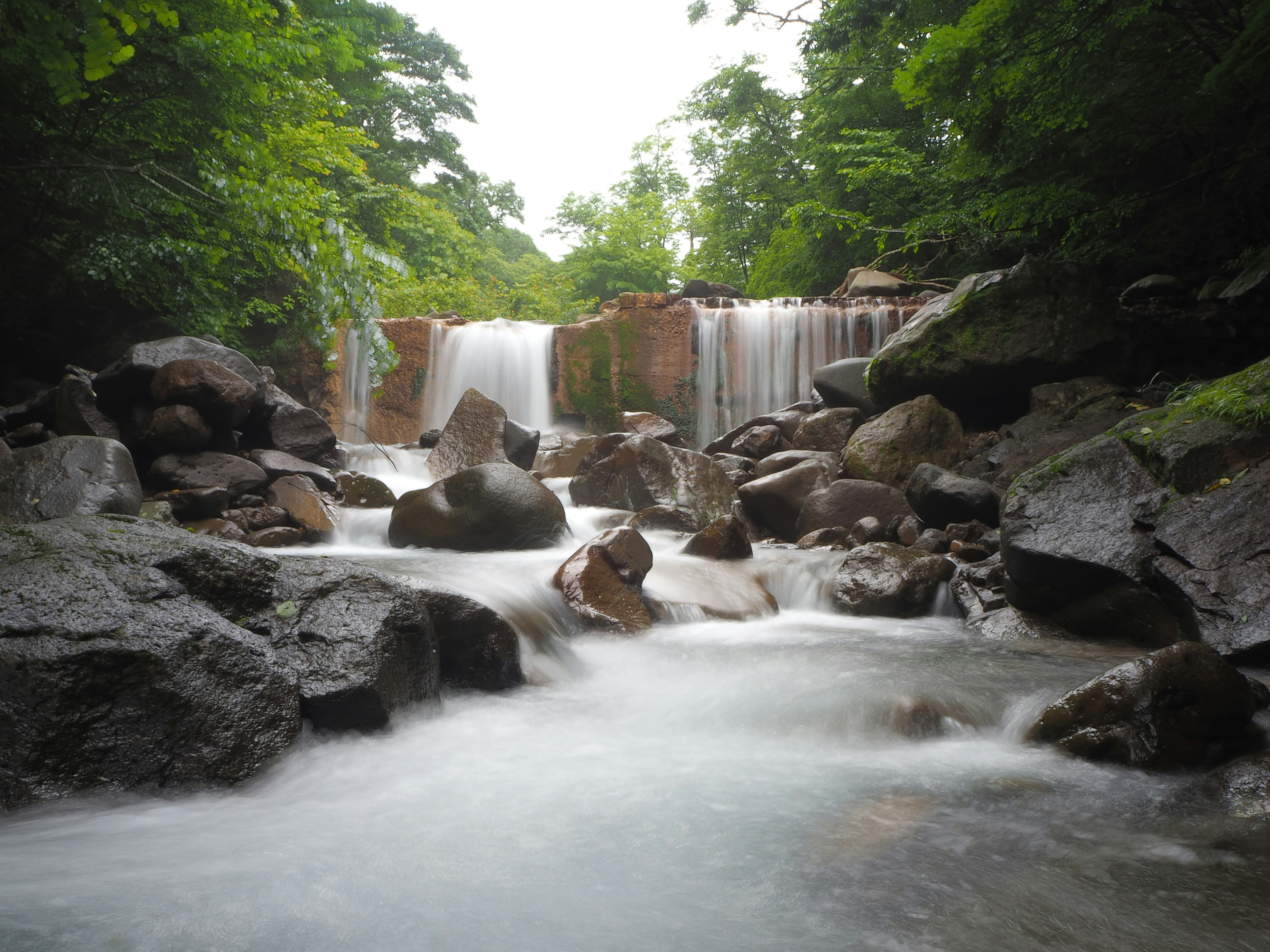 Pemandangan indah air terjun dikelilingi oleh pepohonan hijau dan air yang mengalir