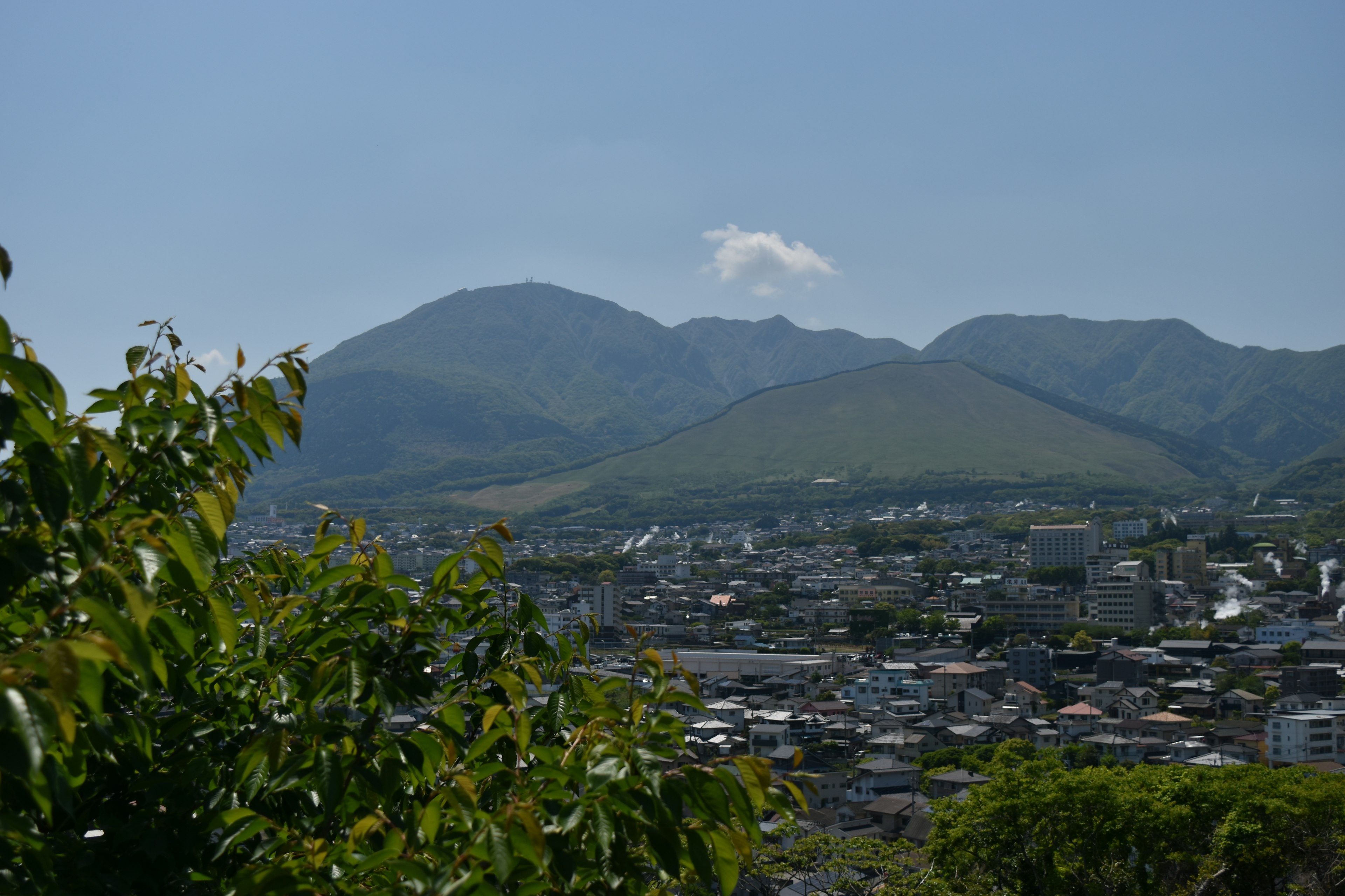 Pemandangan gunung dan kota dengan dedaunan hijau dan langit biru