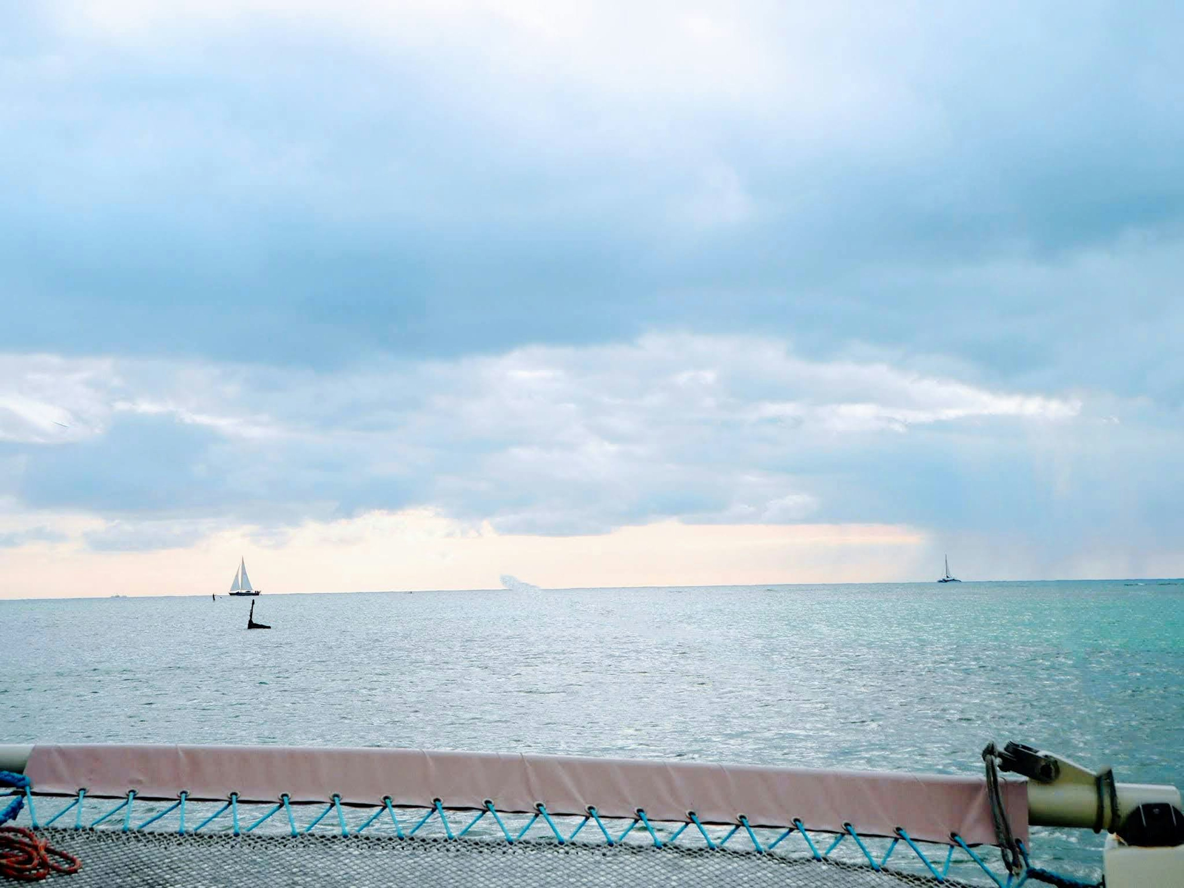 Ruhiges Meer mit bewölktem Himmel und kleinen Segelbooten in der Ferne