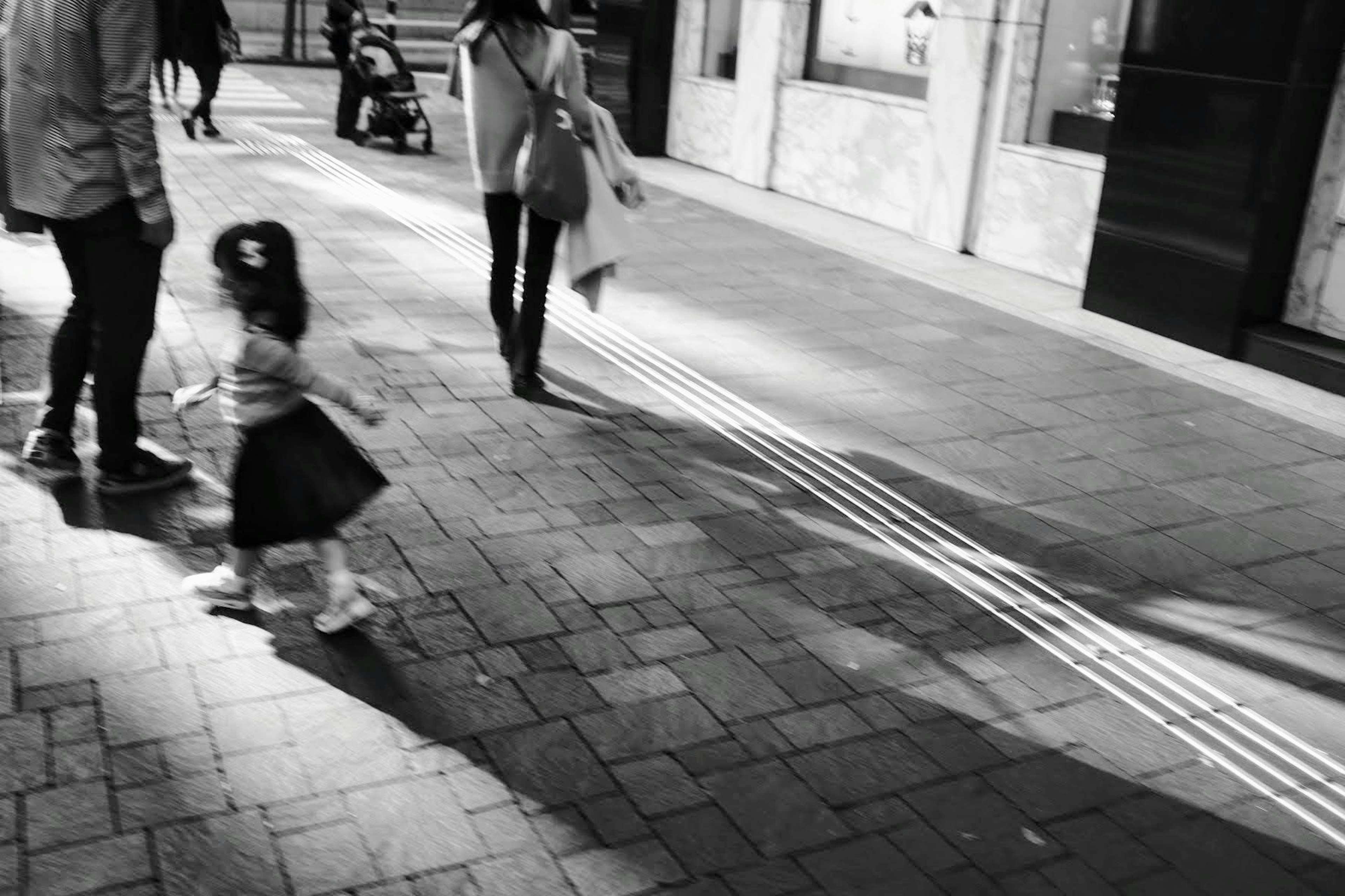 A small girl playing on a city street with pedestrians