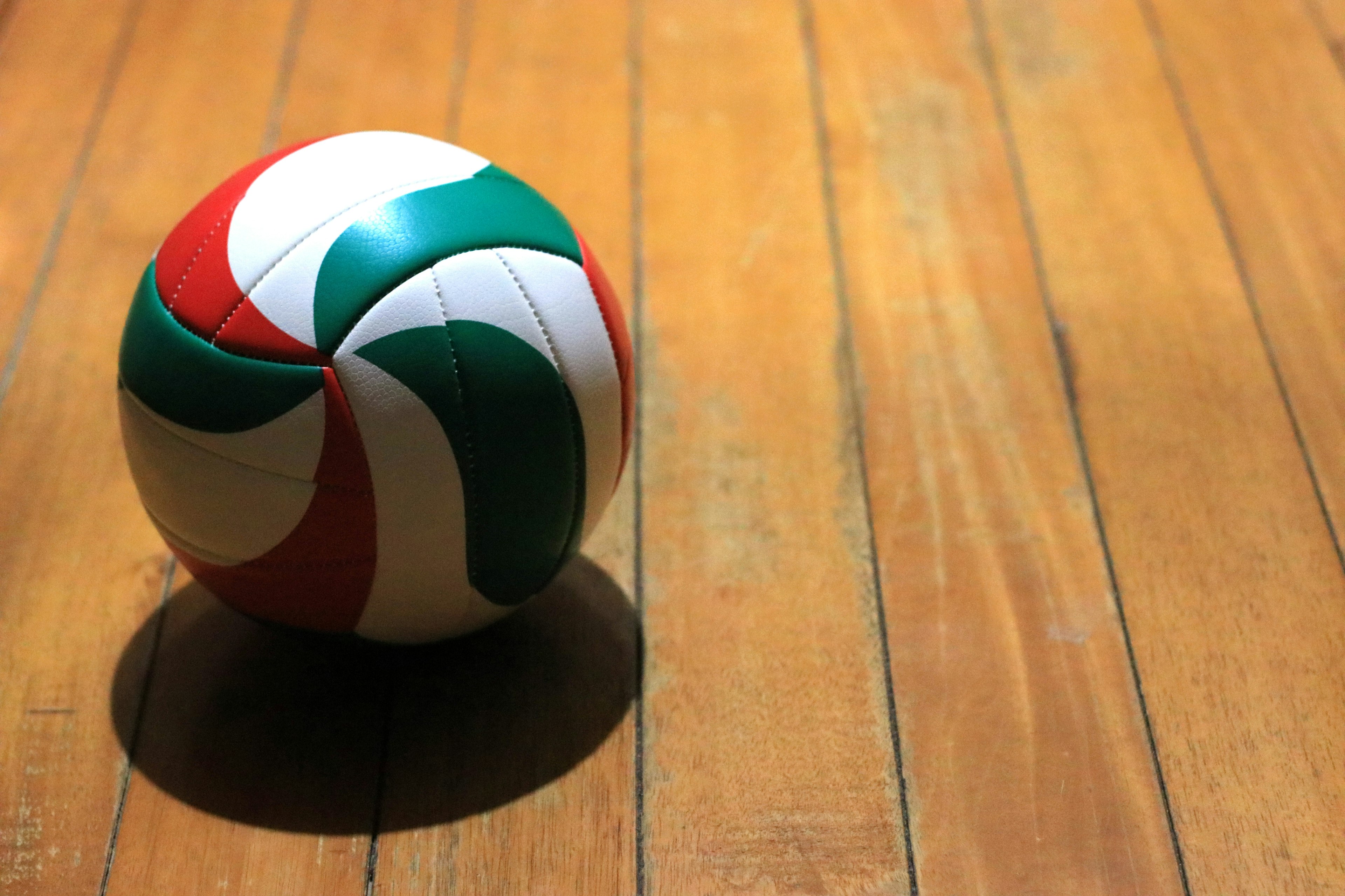 A green and red volleyball on a wooden floor