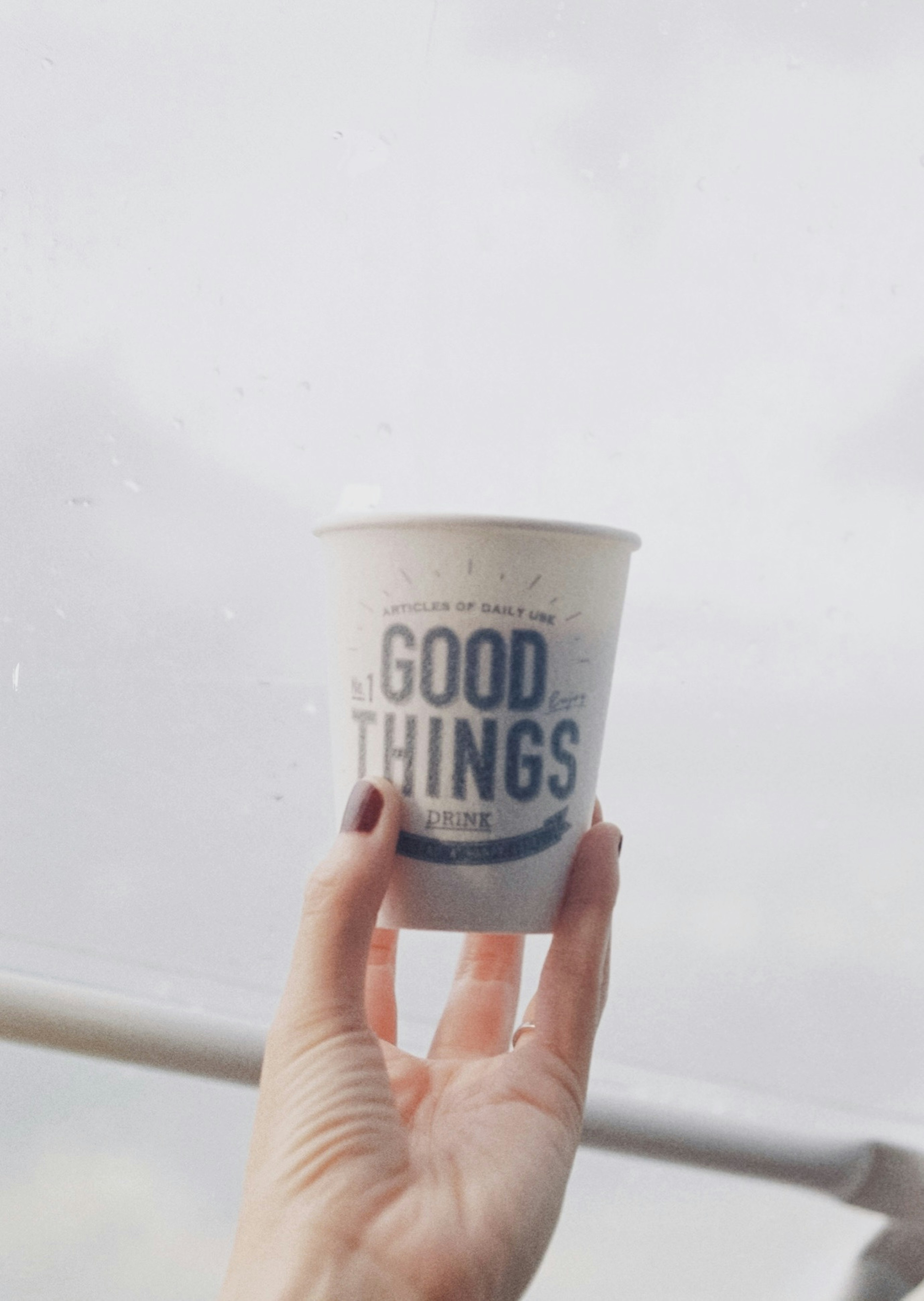 A hand holding a white paper cup with the words GOOD THINGS printed on it