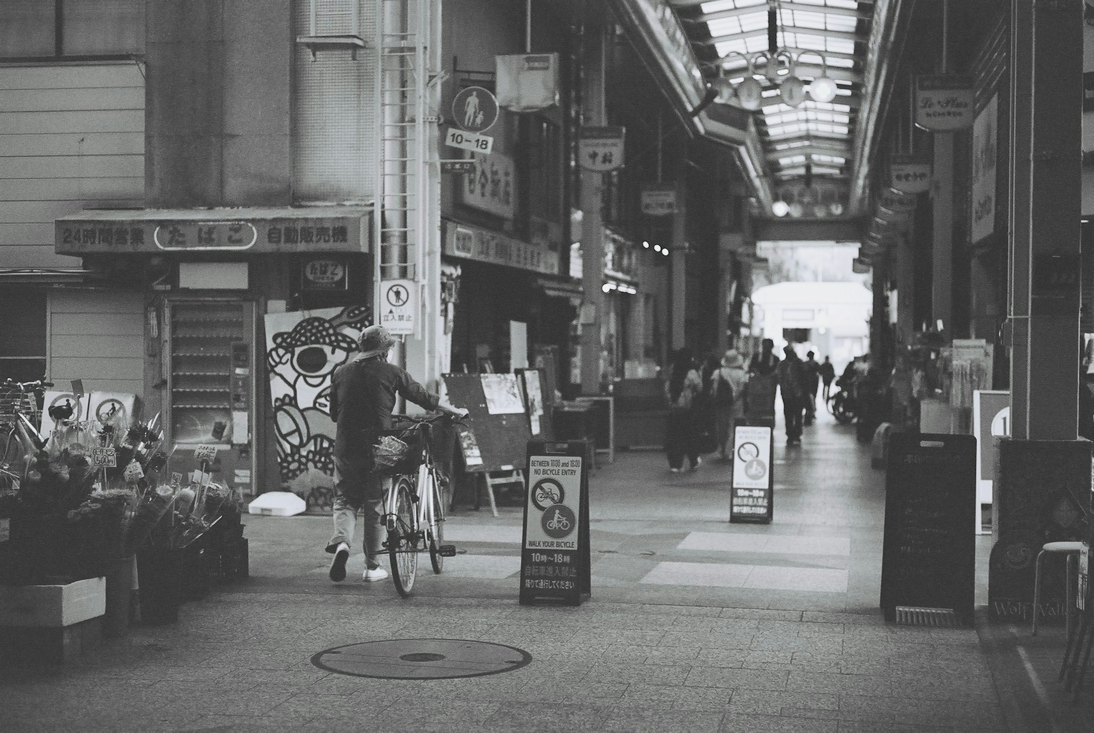 A man riding a bicycle in a bustling shopping arcade with pedestrians