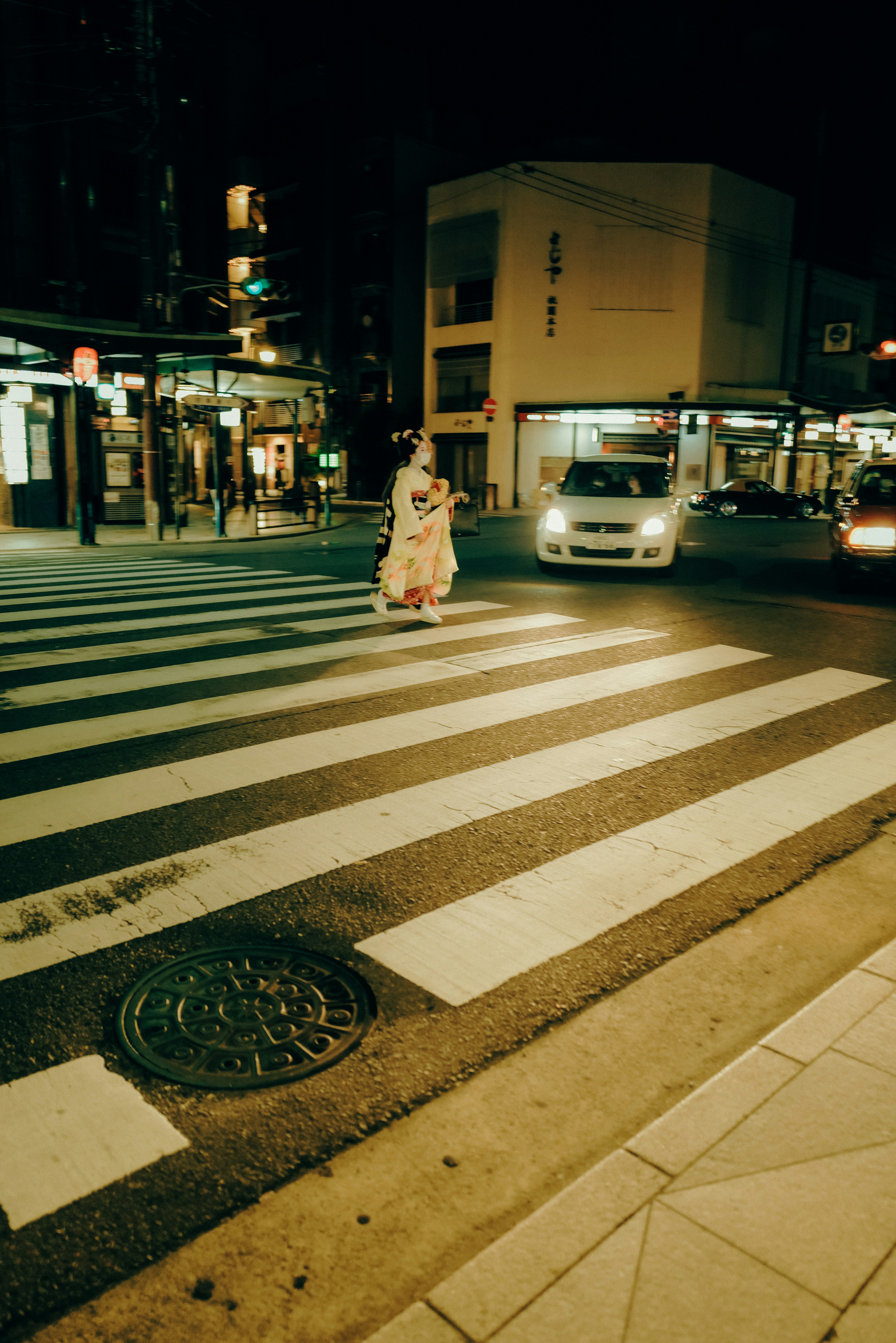 A person in a kimono crossing a street at night with cars