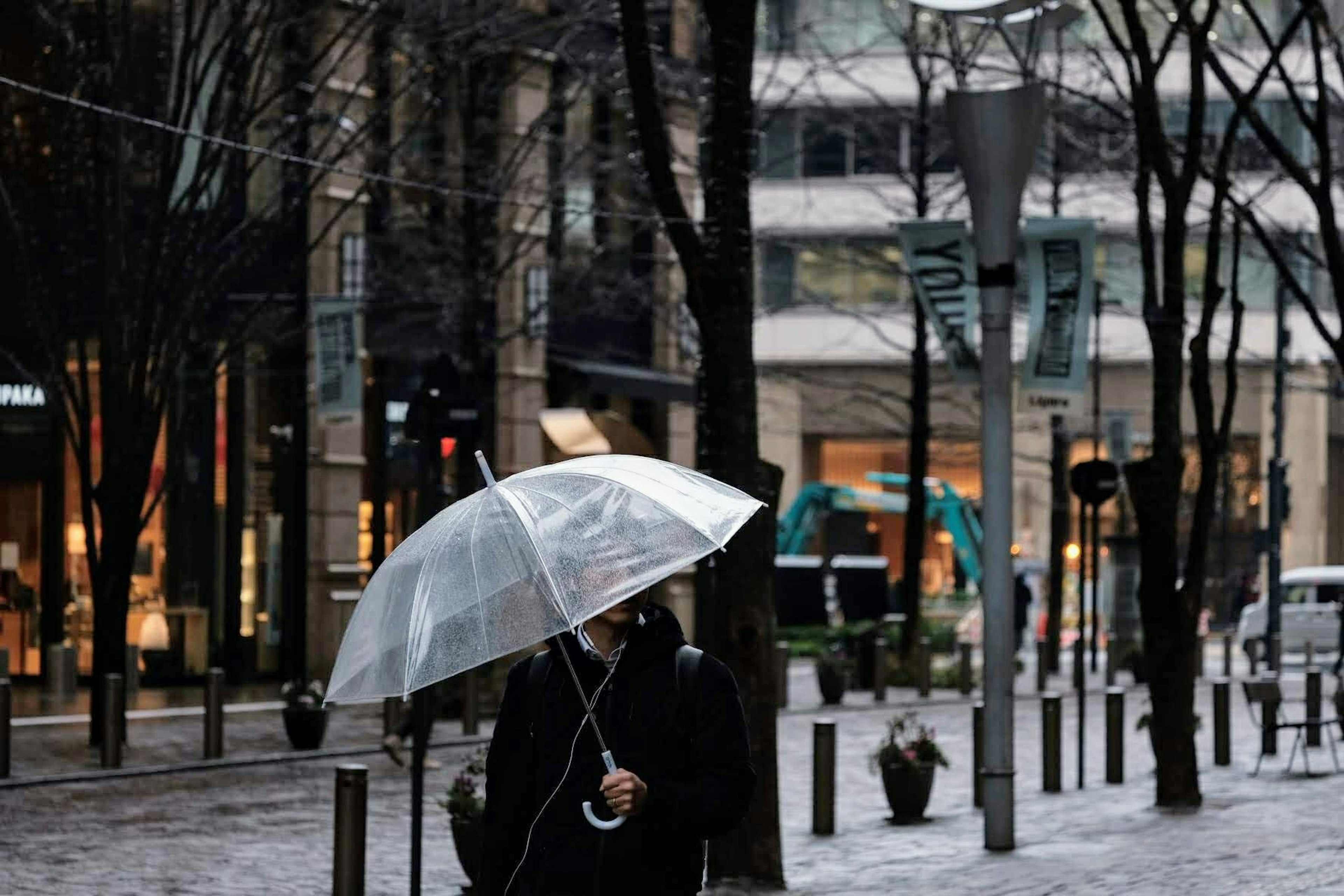 一個人在城市中雨中走著，手持透明傘