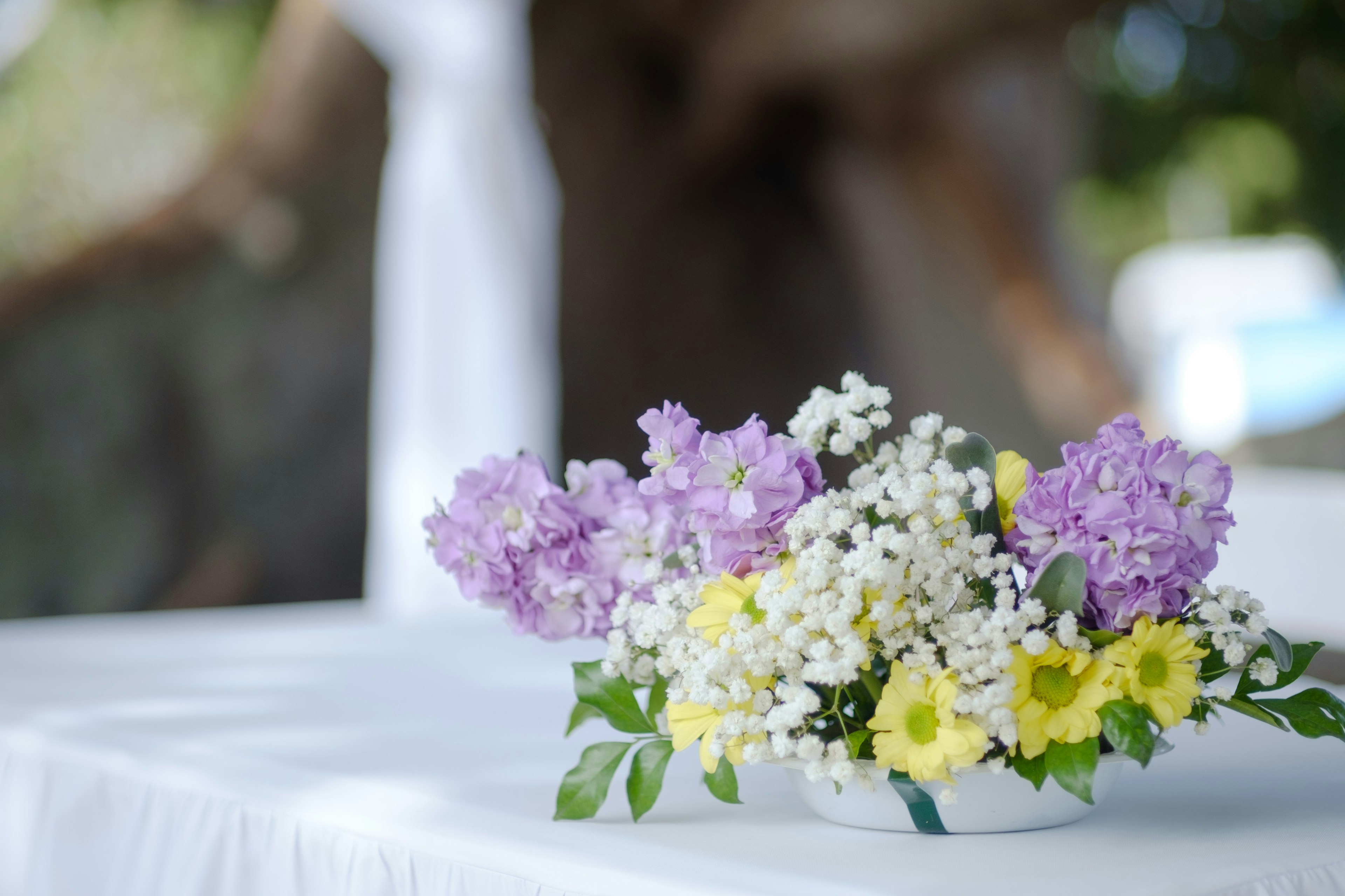 白いテーブルクロスの上にある紫色と黄色の花のアレンジメント