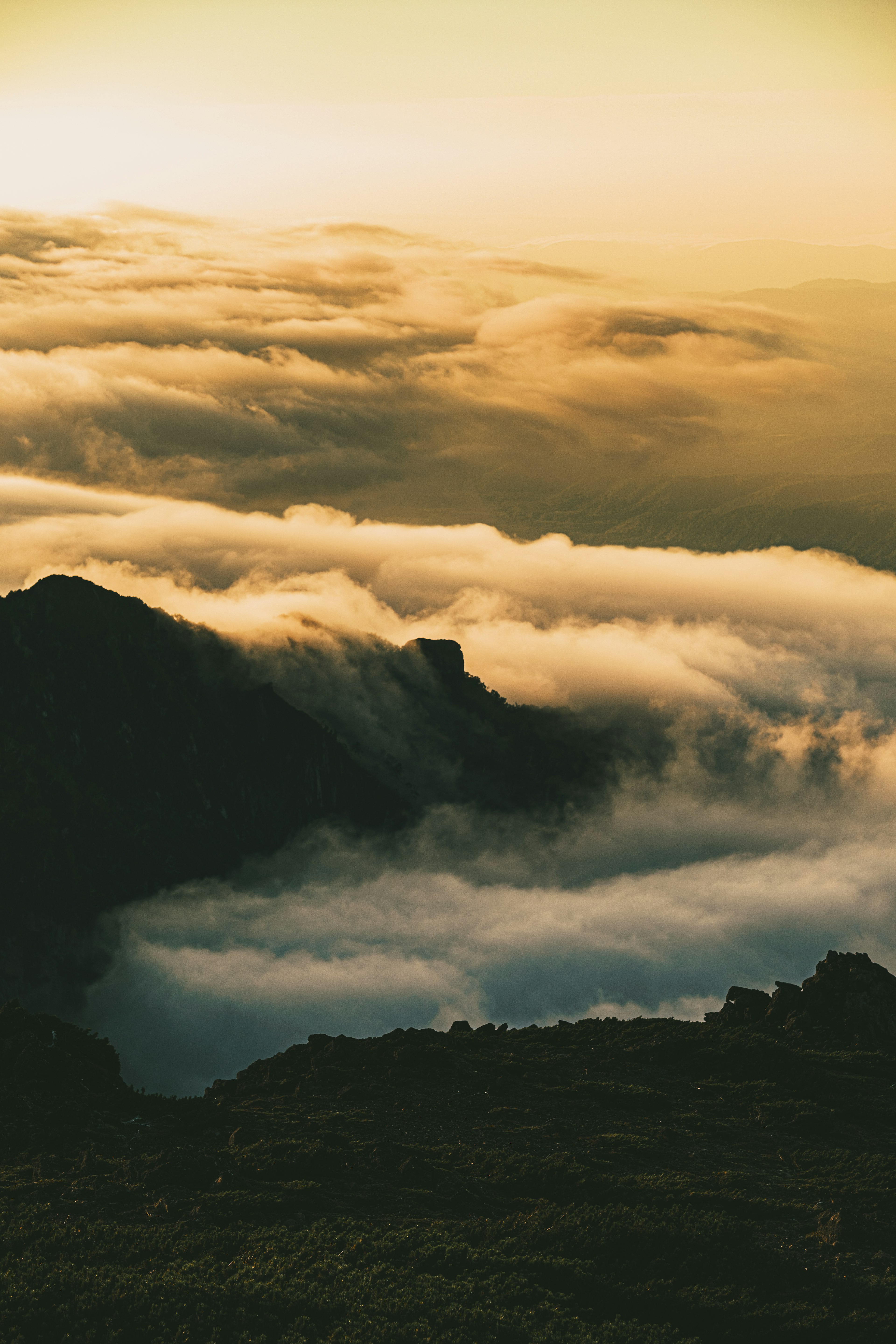 Silueta de montañas cubiertas por un mar de nubes con un suave resplandor crepuscular