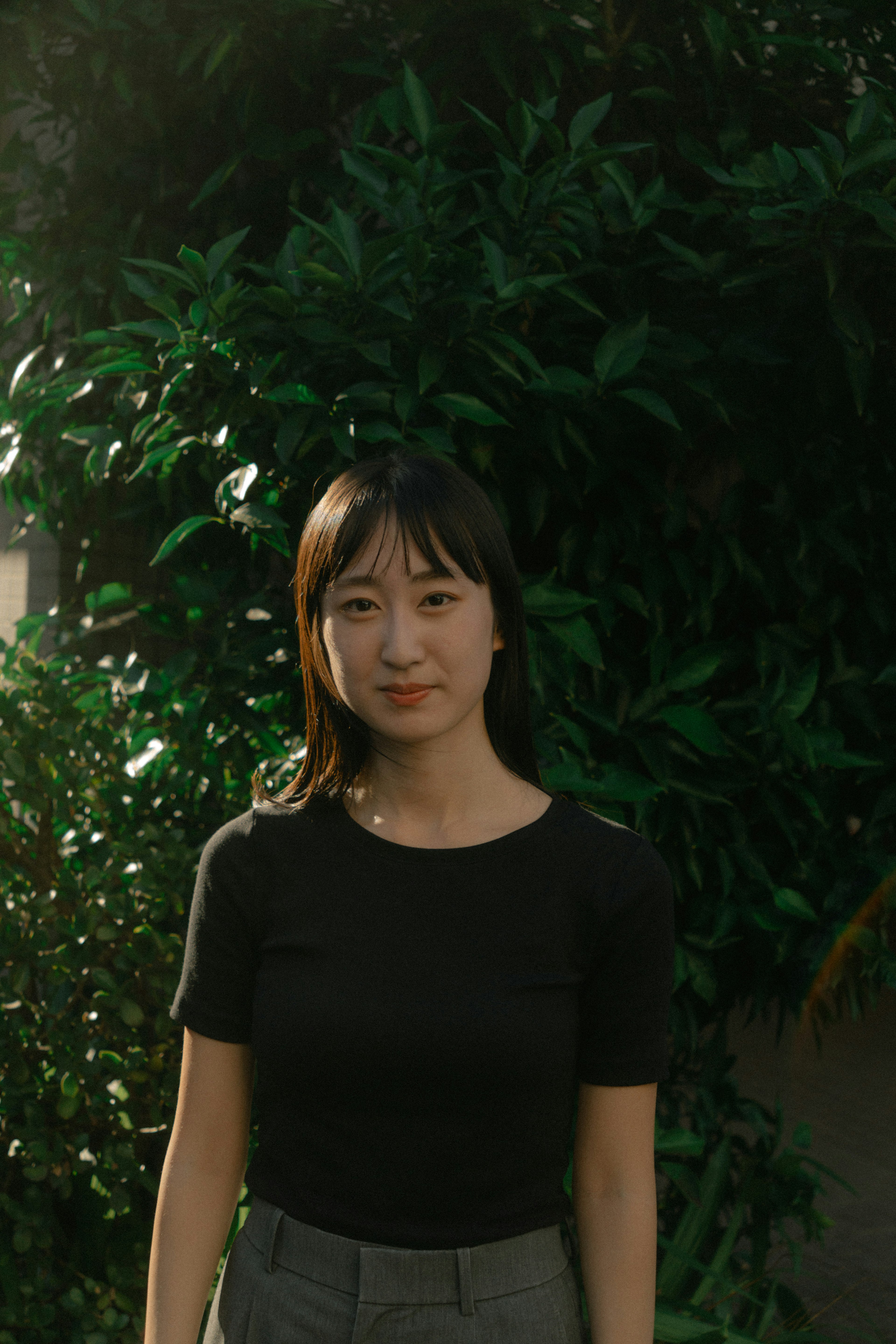 Portrait of a woman standing against a green leafy background