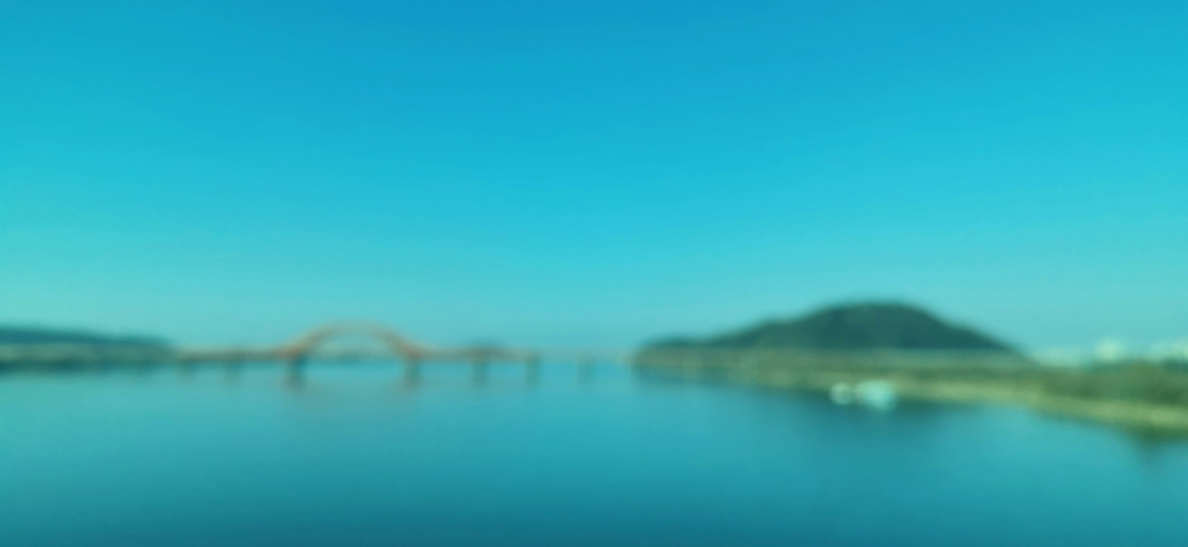 Vista escénica con cielo azul y agua tranquila con un puente y una colina