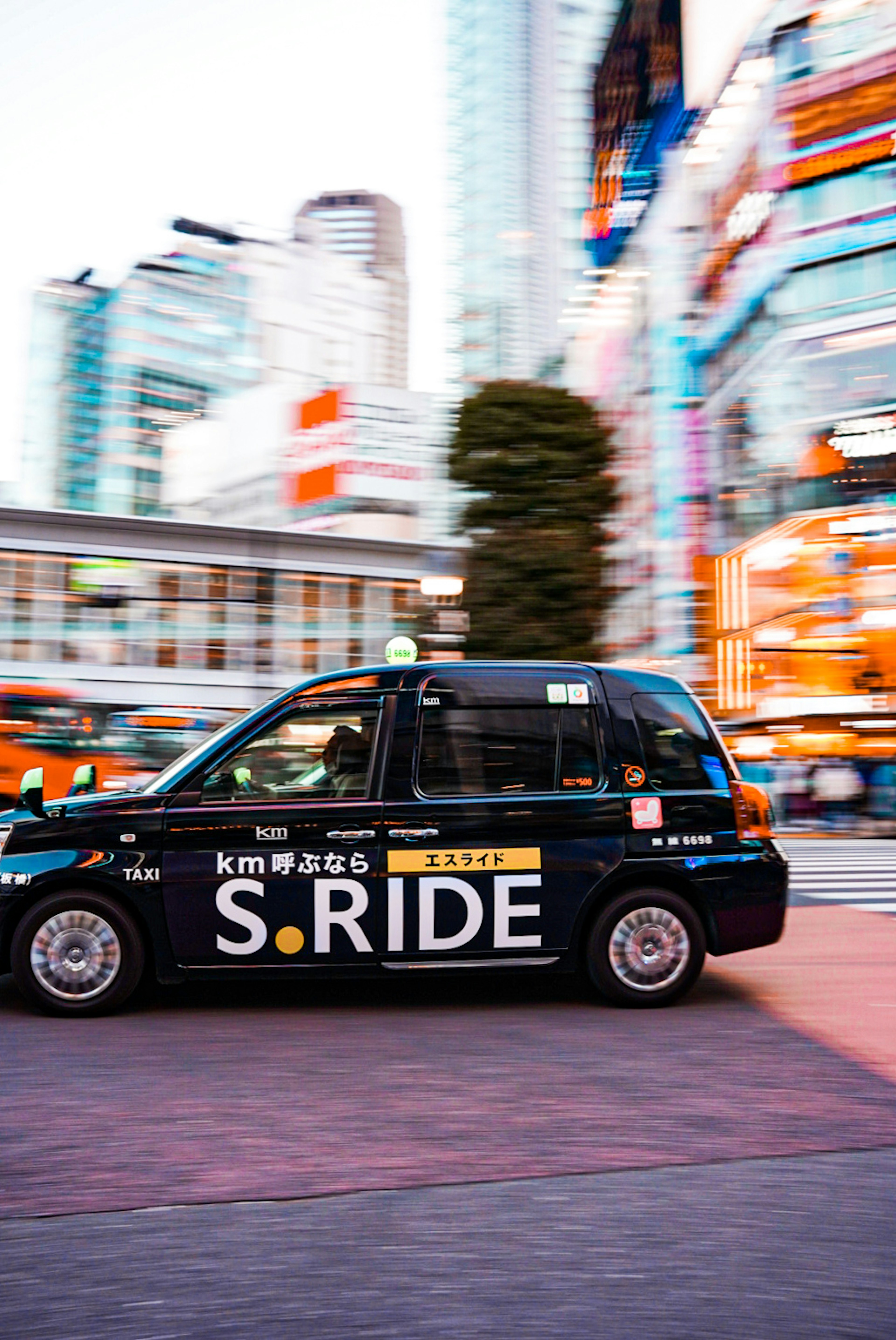 Black taxi with S.RIDE logo moving through Tokyo cityscape