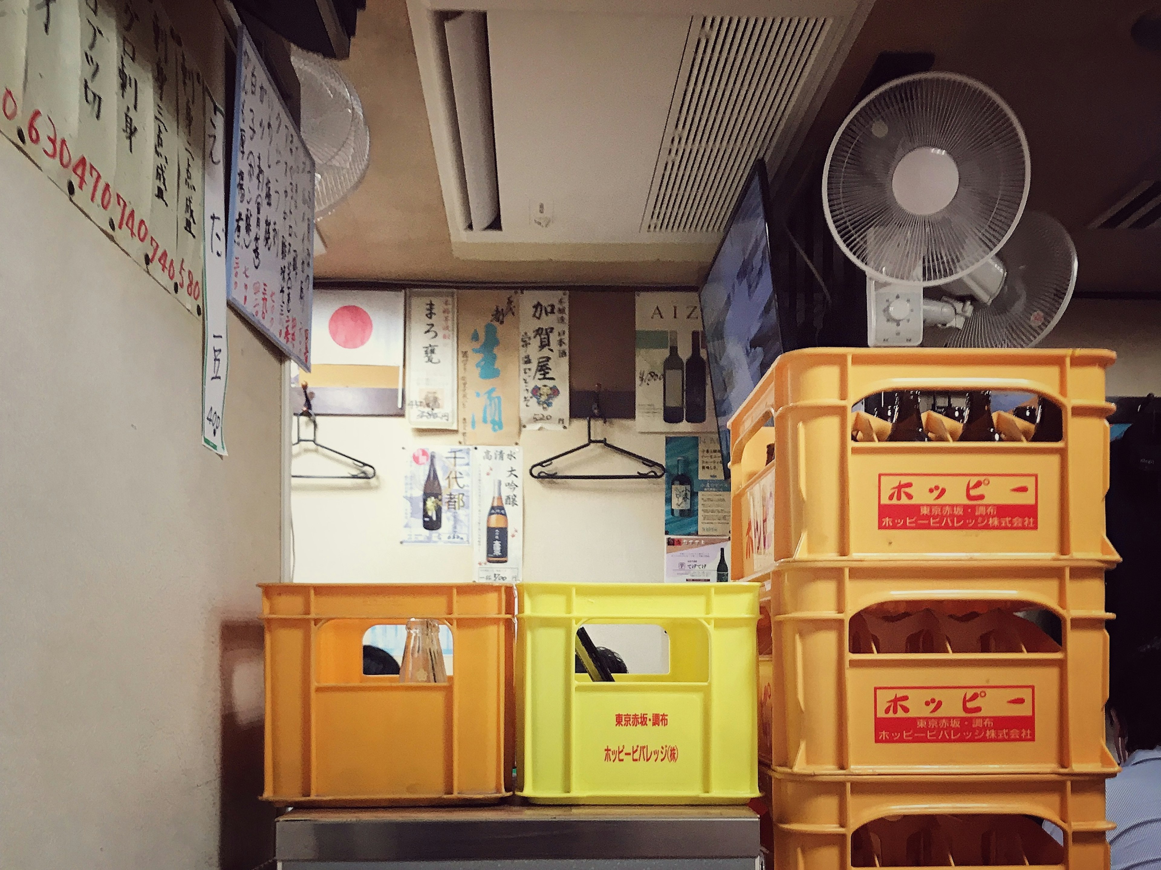 Cajas de plástico naranjas y amarillas apiladas con carteles japoneses y ventiladores en la pared