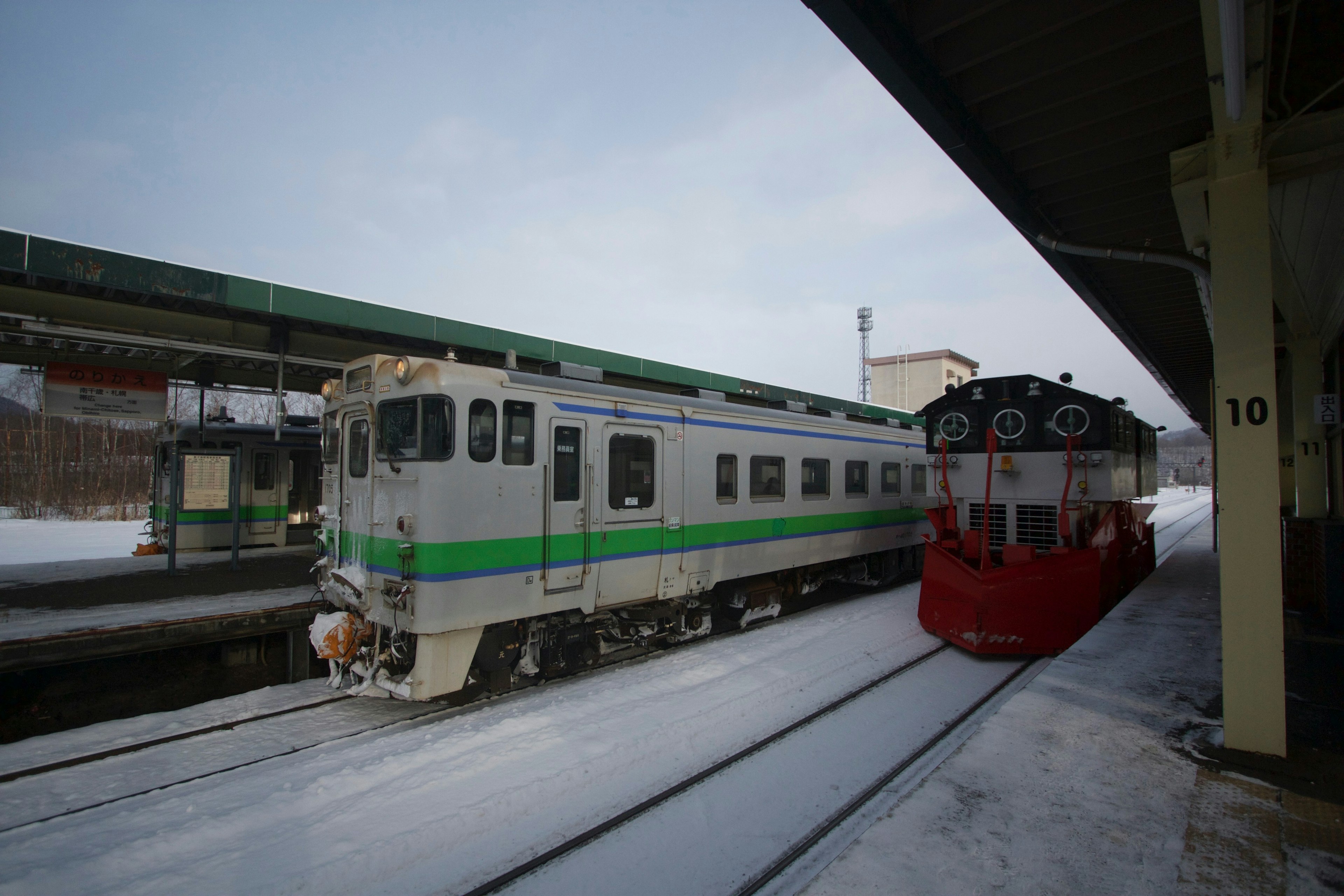 雪に覆われた駅で停車中の緑と白の列車と赤い機関車