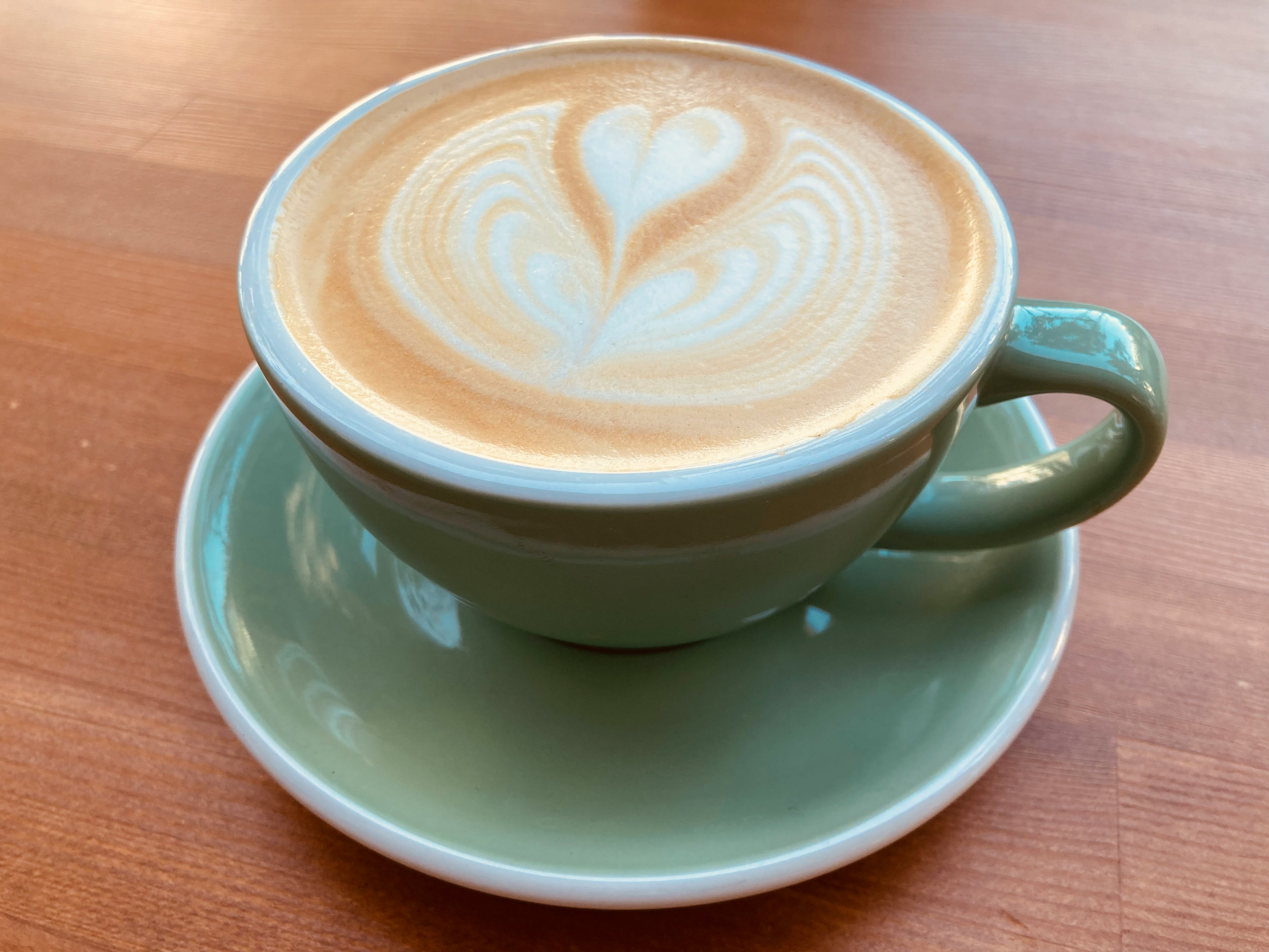 Caffè in una tazza verde con arte del latte cremosa a forma di cuore