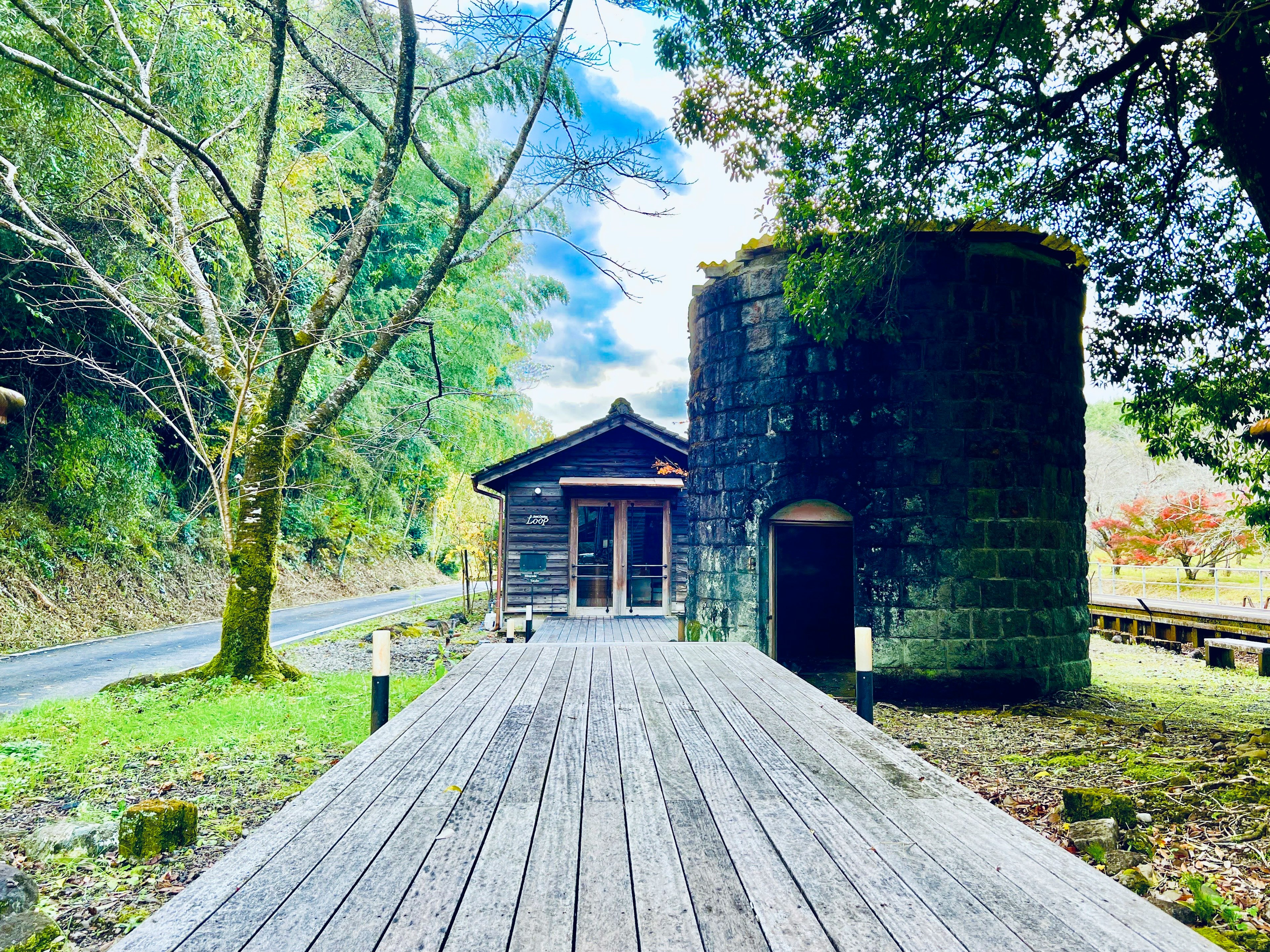 Landscape featuring a small stone building and cylindrical structure surrounded by wooden decking