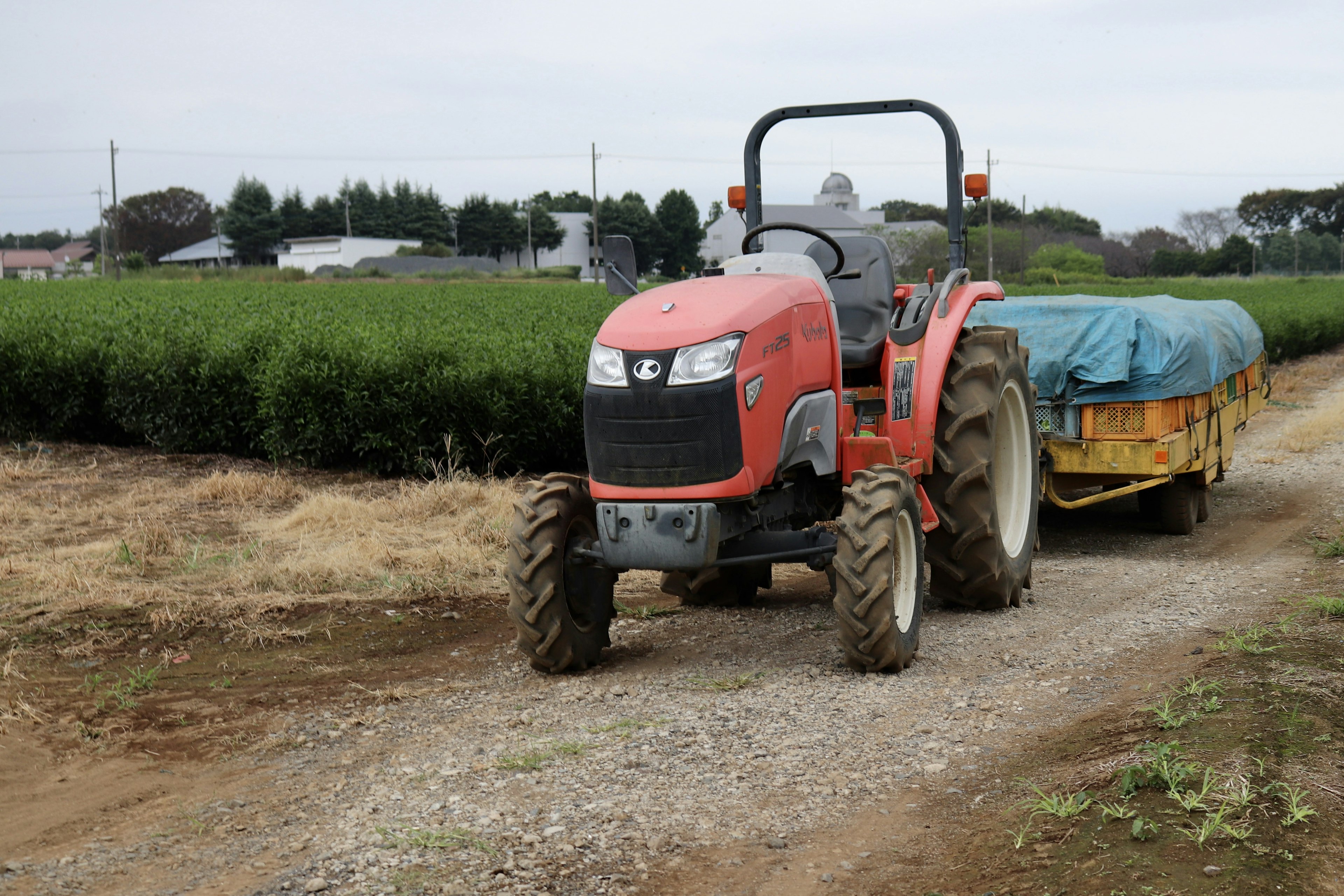 Tractor rojo con remolque azul en un camino de grava