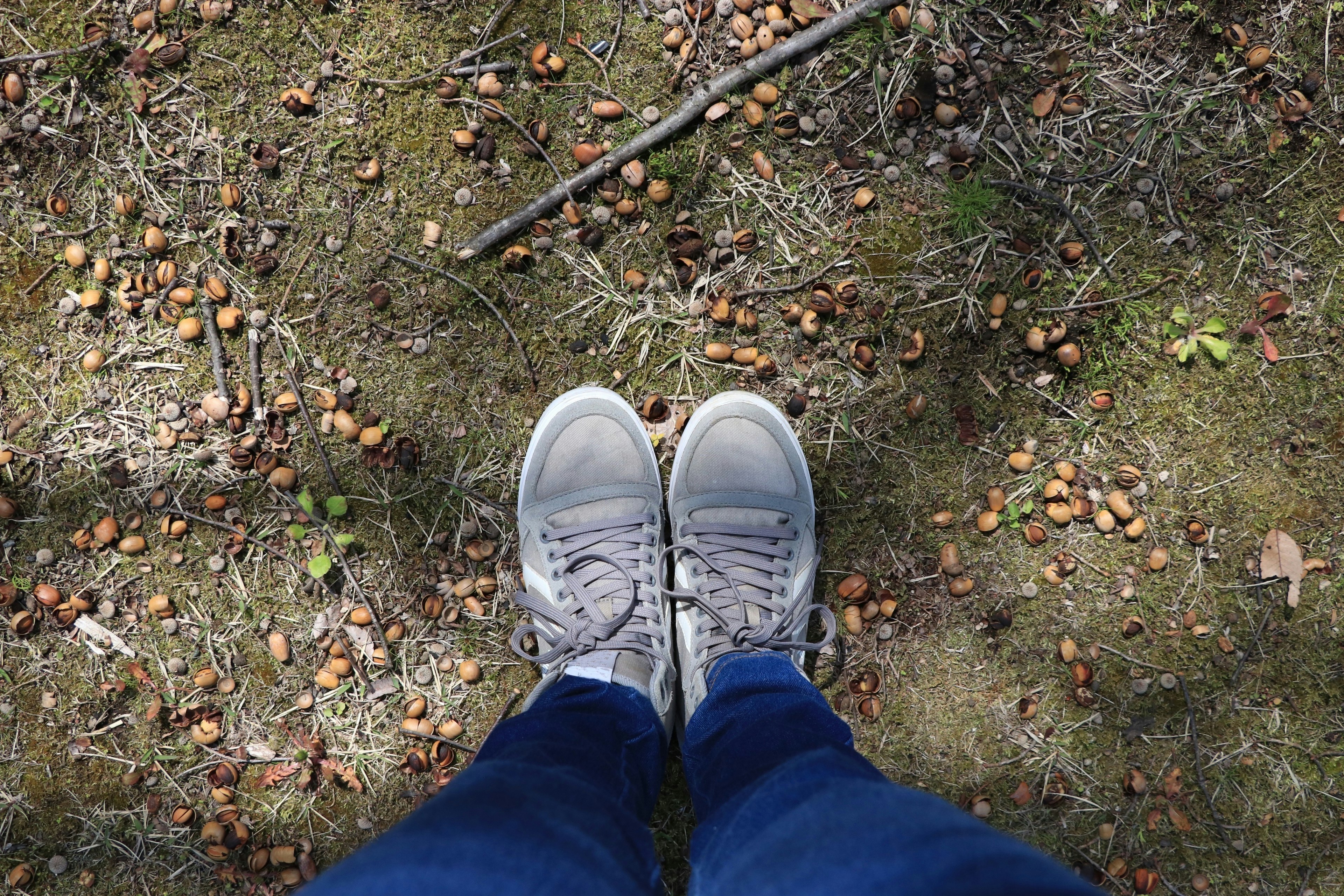 Gray sneakers and blue jeans are visible at the feet with scattered leaves and small twigs around