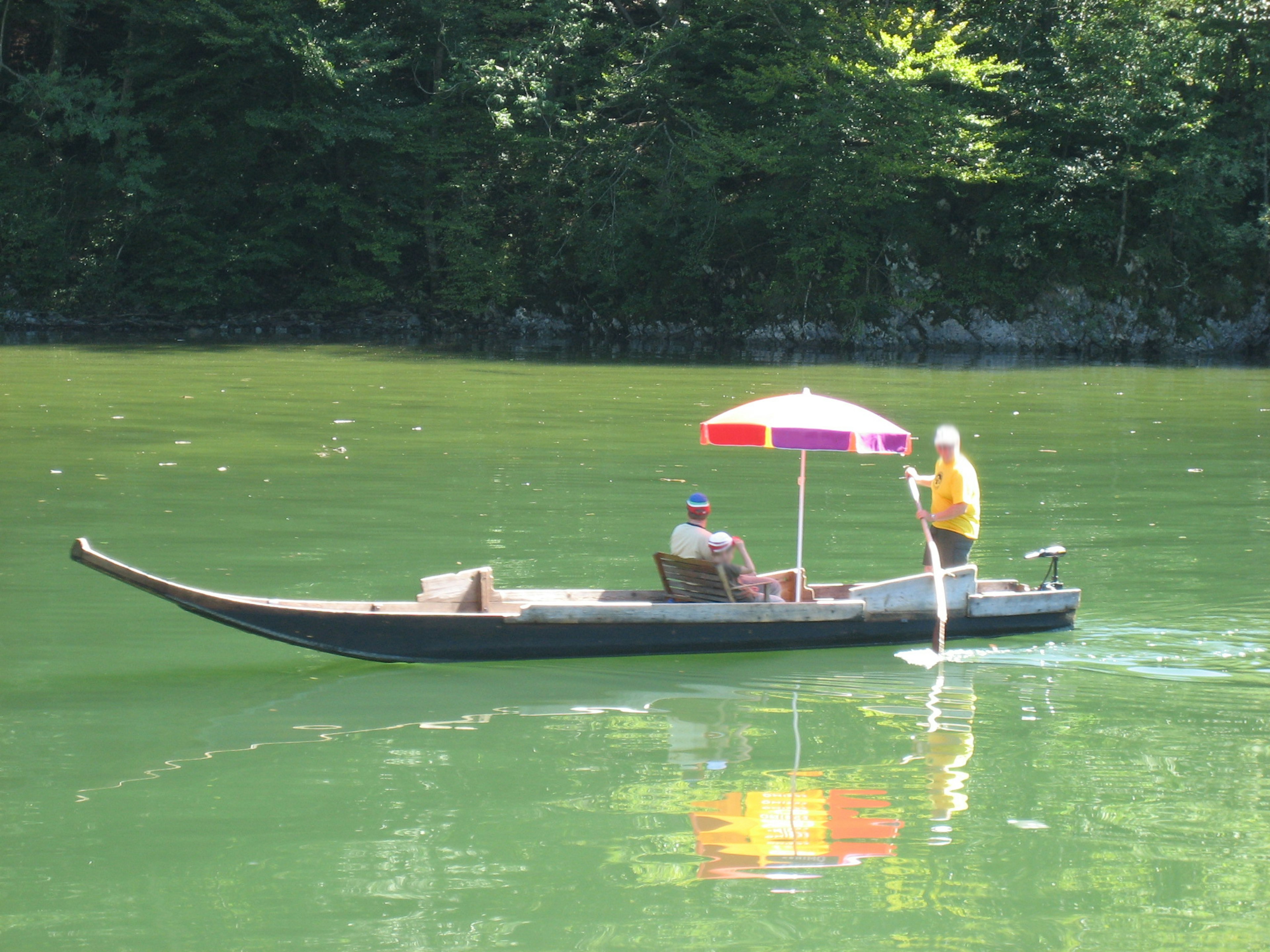 Barca sull'acqua verde con un rematore che tiene un ombrello colorato