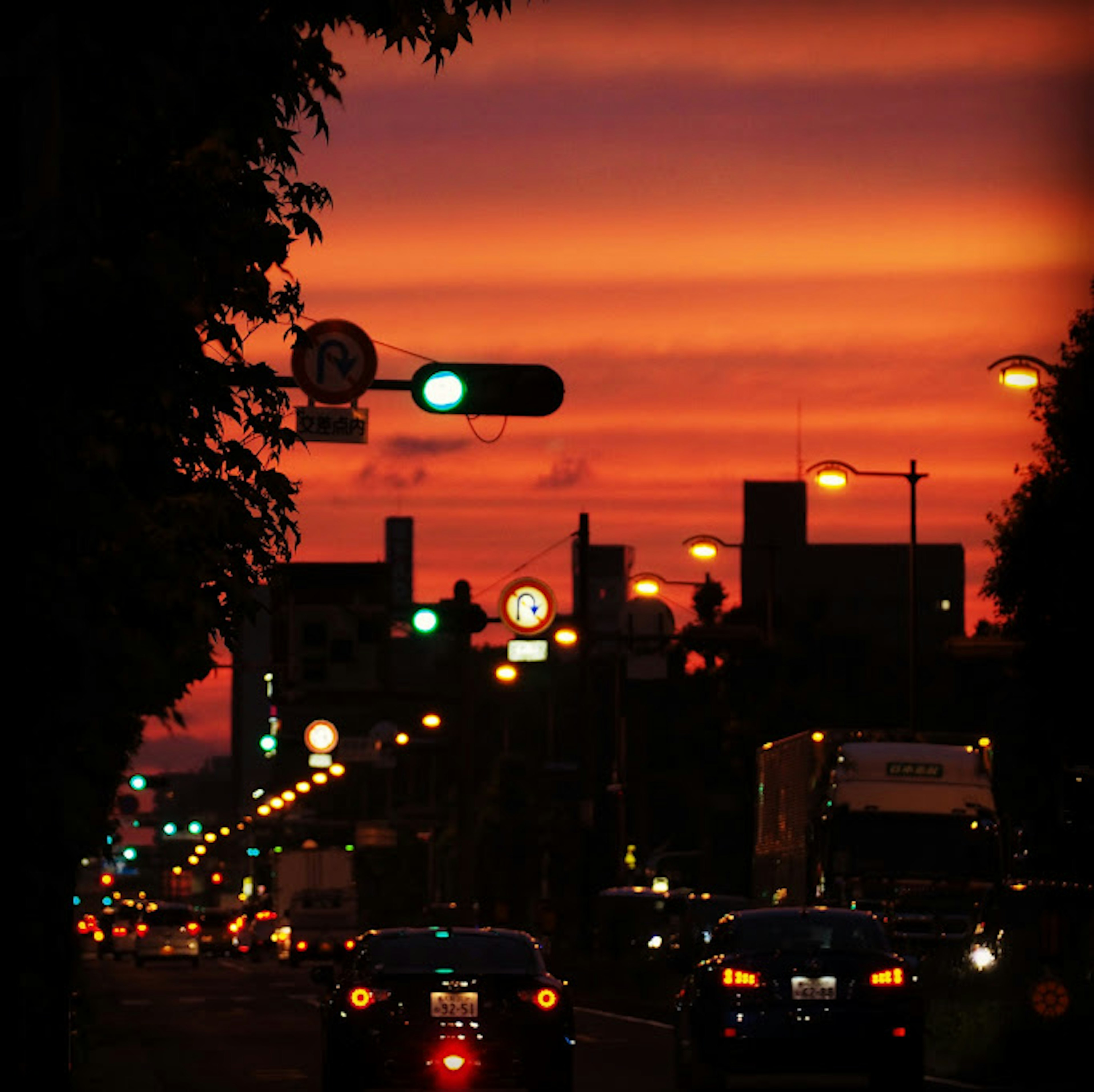 Cityscape at sunset with vibrant red and orange sky featuring traffic lights and vehicles