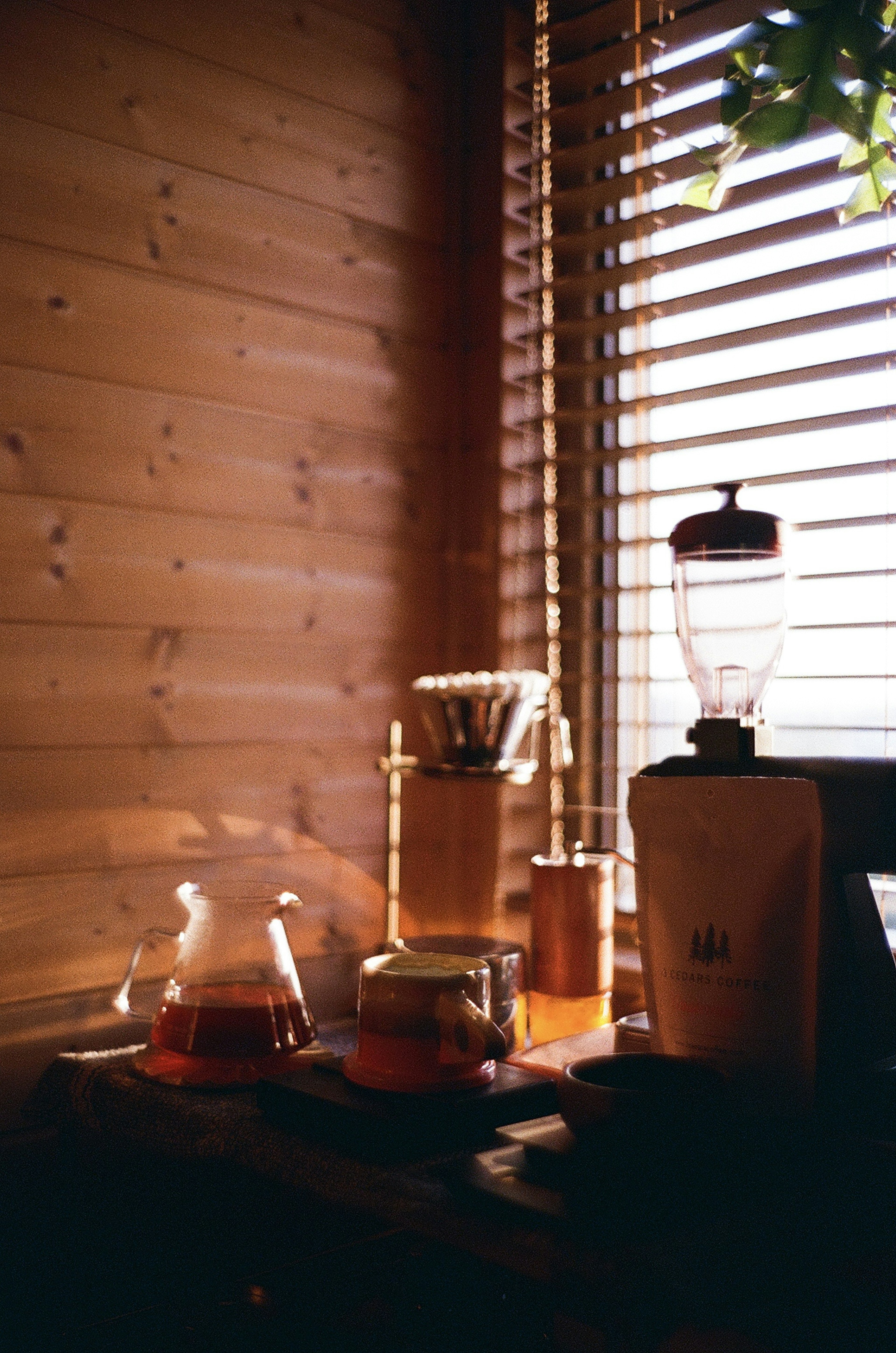 A cozy scene featuring teapots and glass containers near a window with wooden walls and blinds warm drink colors