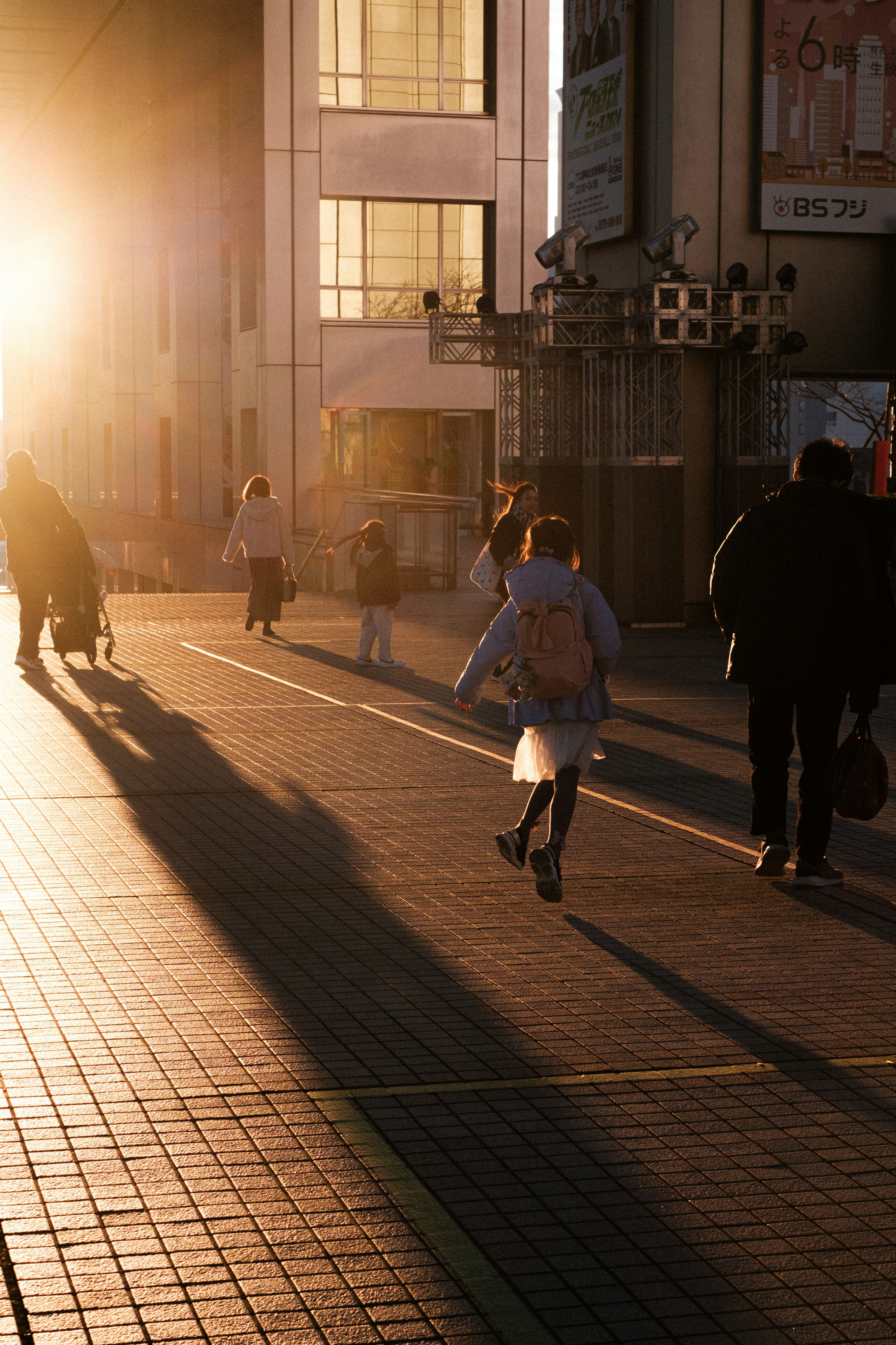 夕日を背にした街の風景を歩く人々や子供の後ろ姿