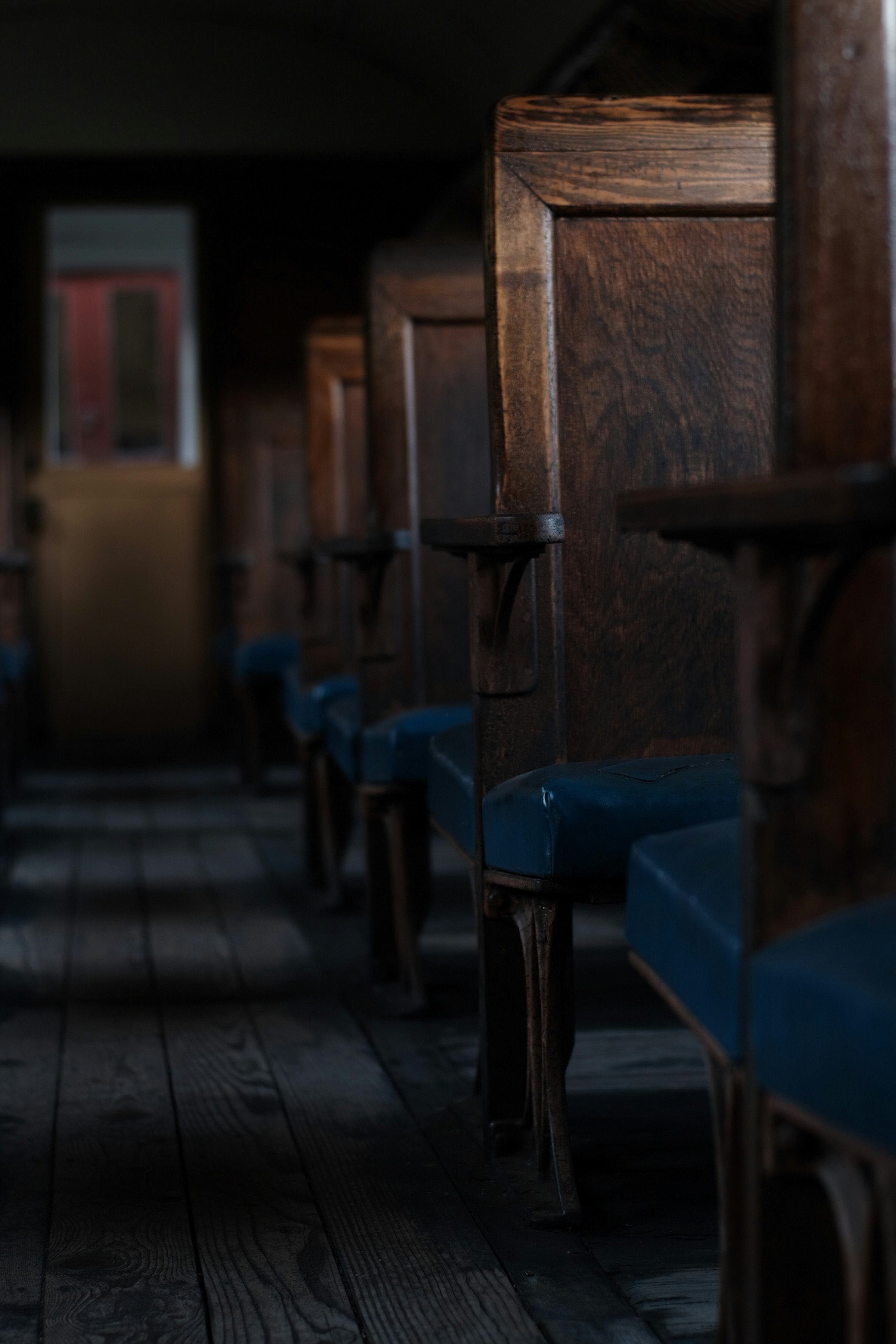 Dimly lit interior featuring rows of wooden chairs with blue upholstery