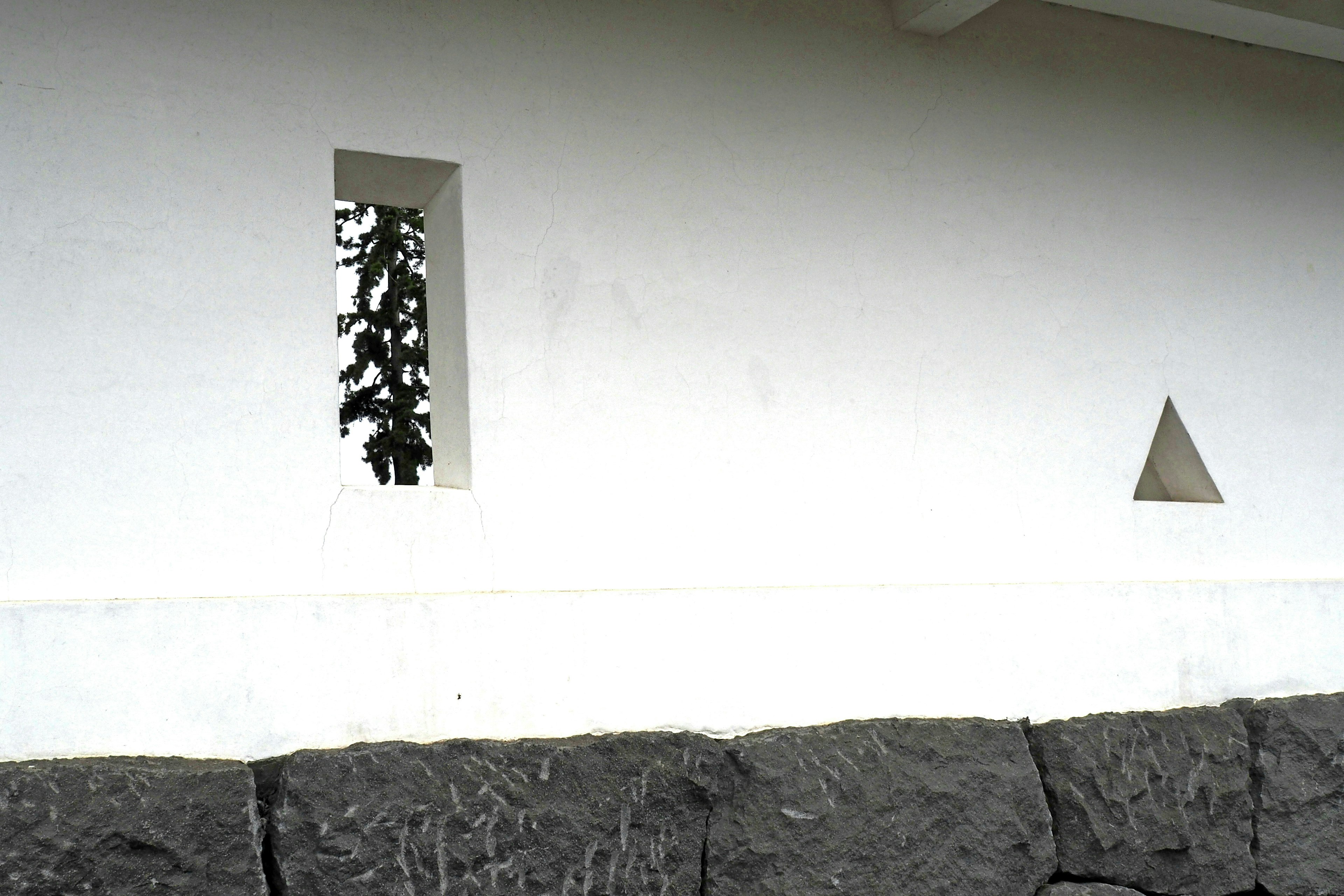 White wall with a rectangular window and triangular opening above a stone foundation