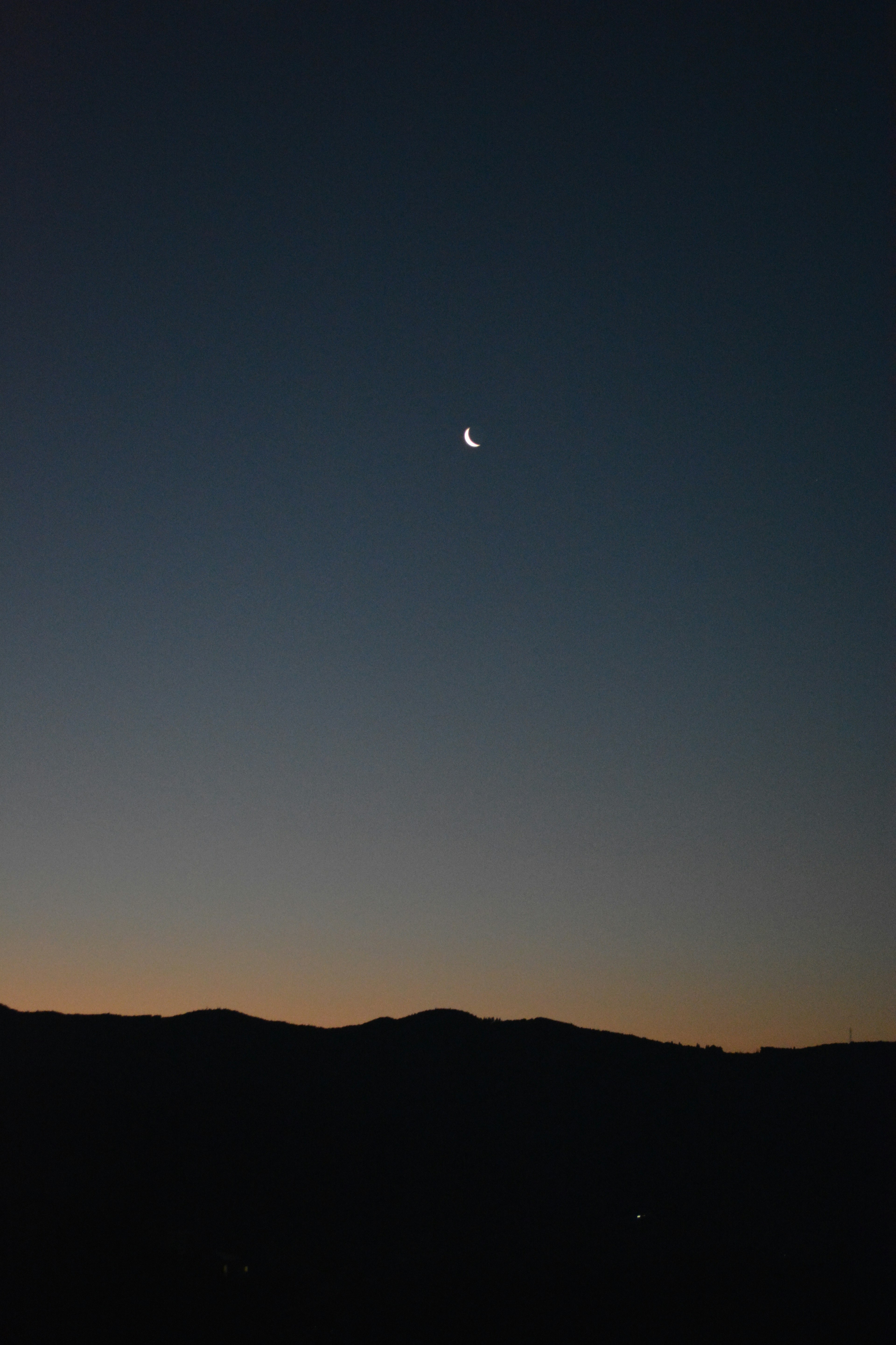 Luna creciente en el cielo nocturno con siluetas de montañas