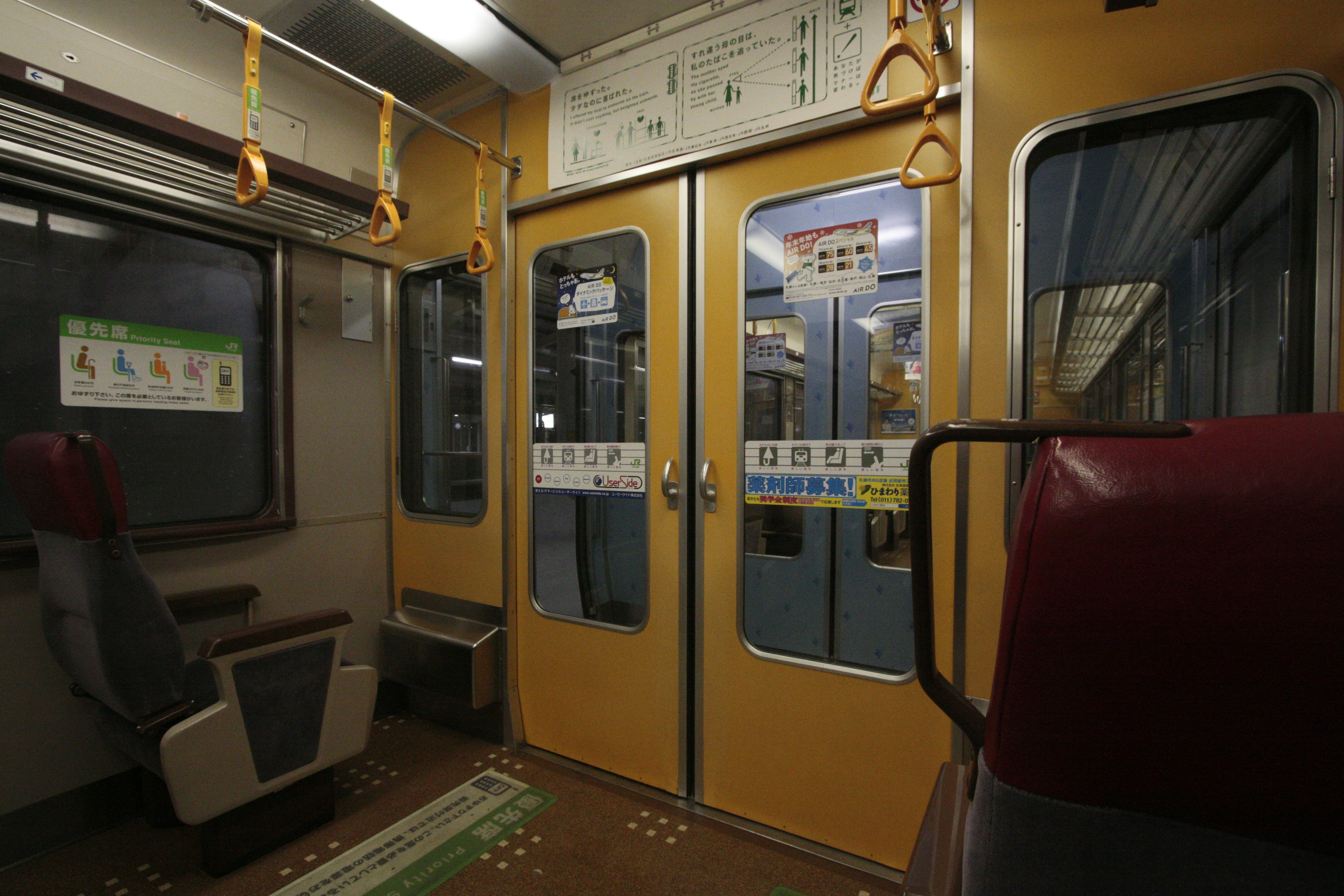 Interior kereta dengan dinding kuning dan tempat duduk tanpa penumpang menciptakan suasana tenang