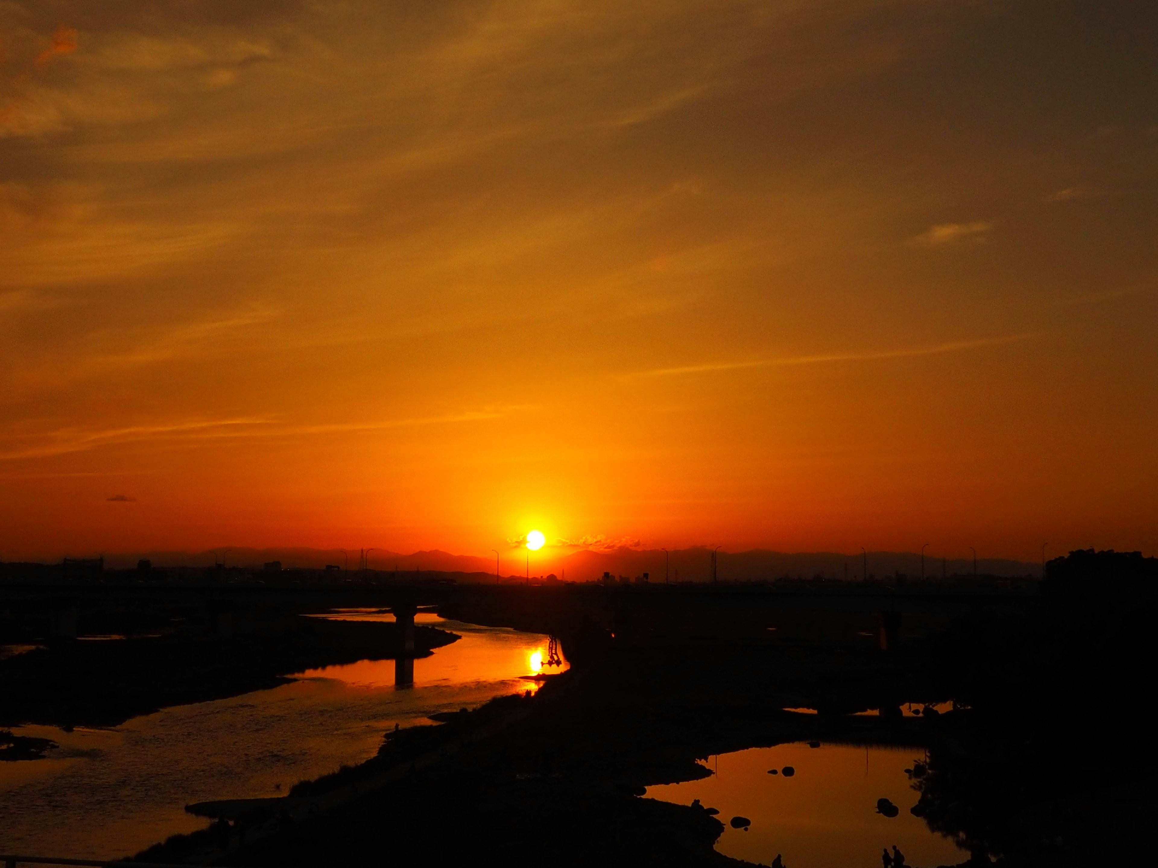 A serene river landscape at sunset with a reflective water surface and an orange sky