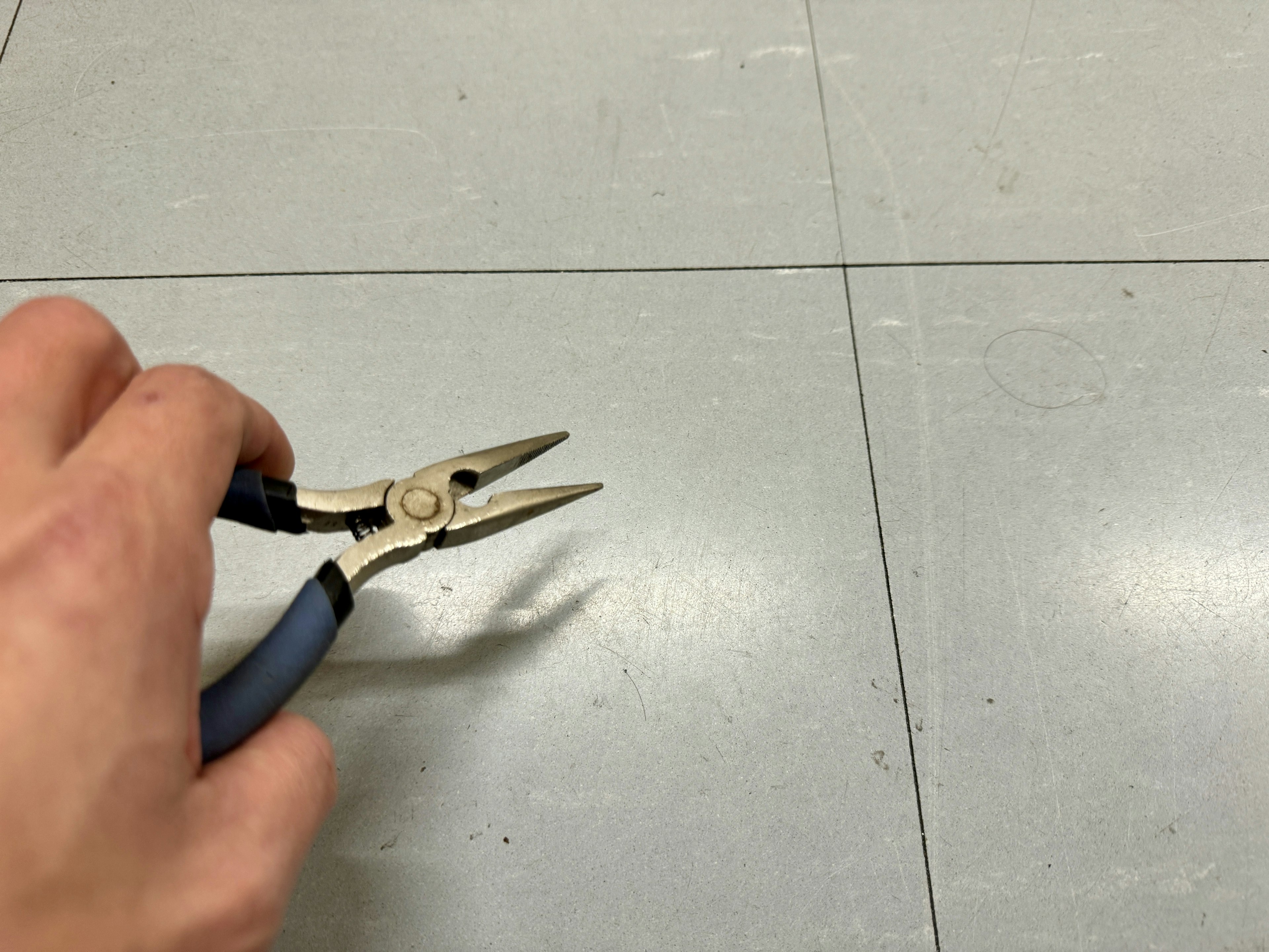 A hand holding pliers over a gray floor