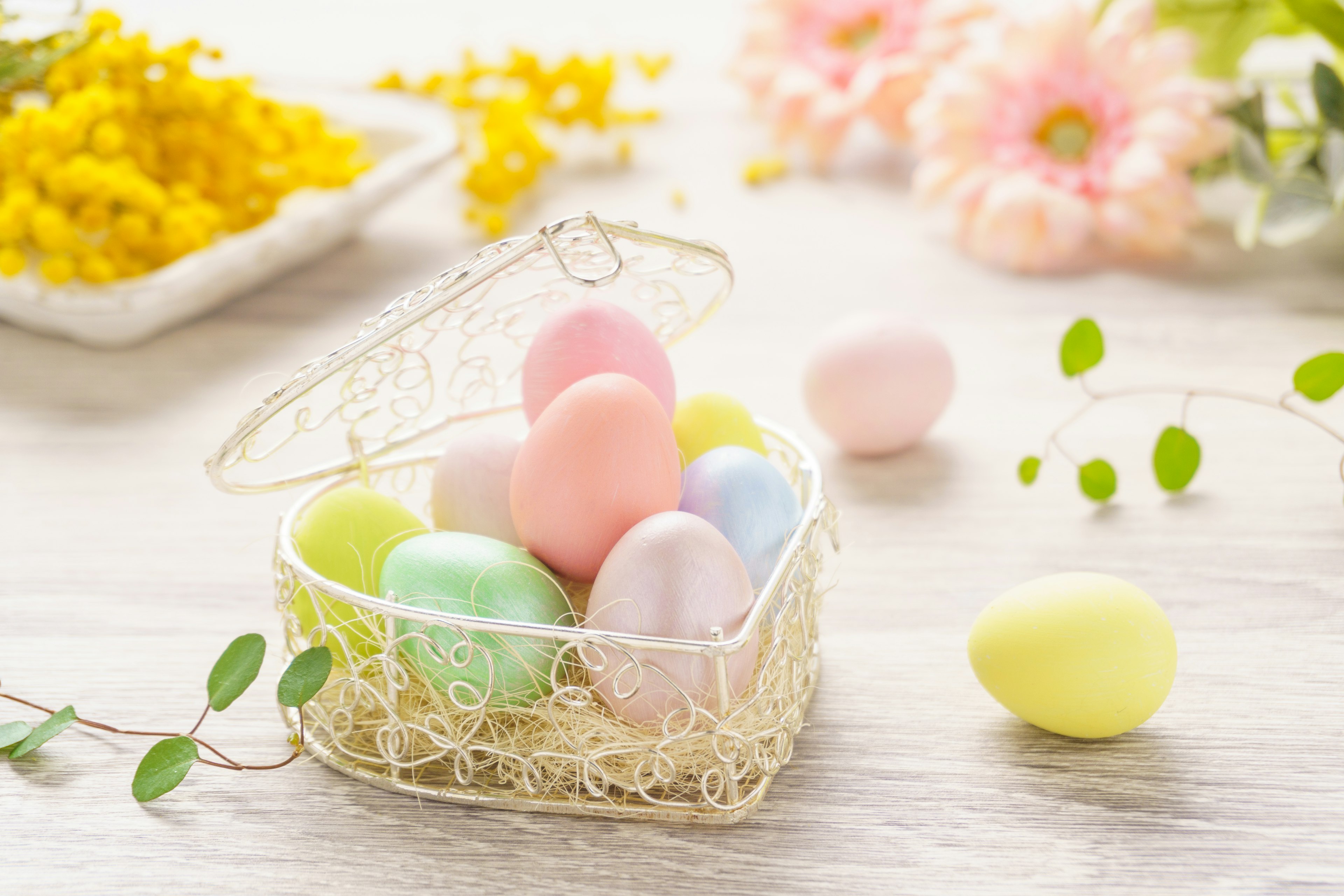 Oeufs colorés dans un panier décoratif avec des fleurs de printemps