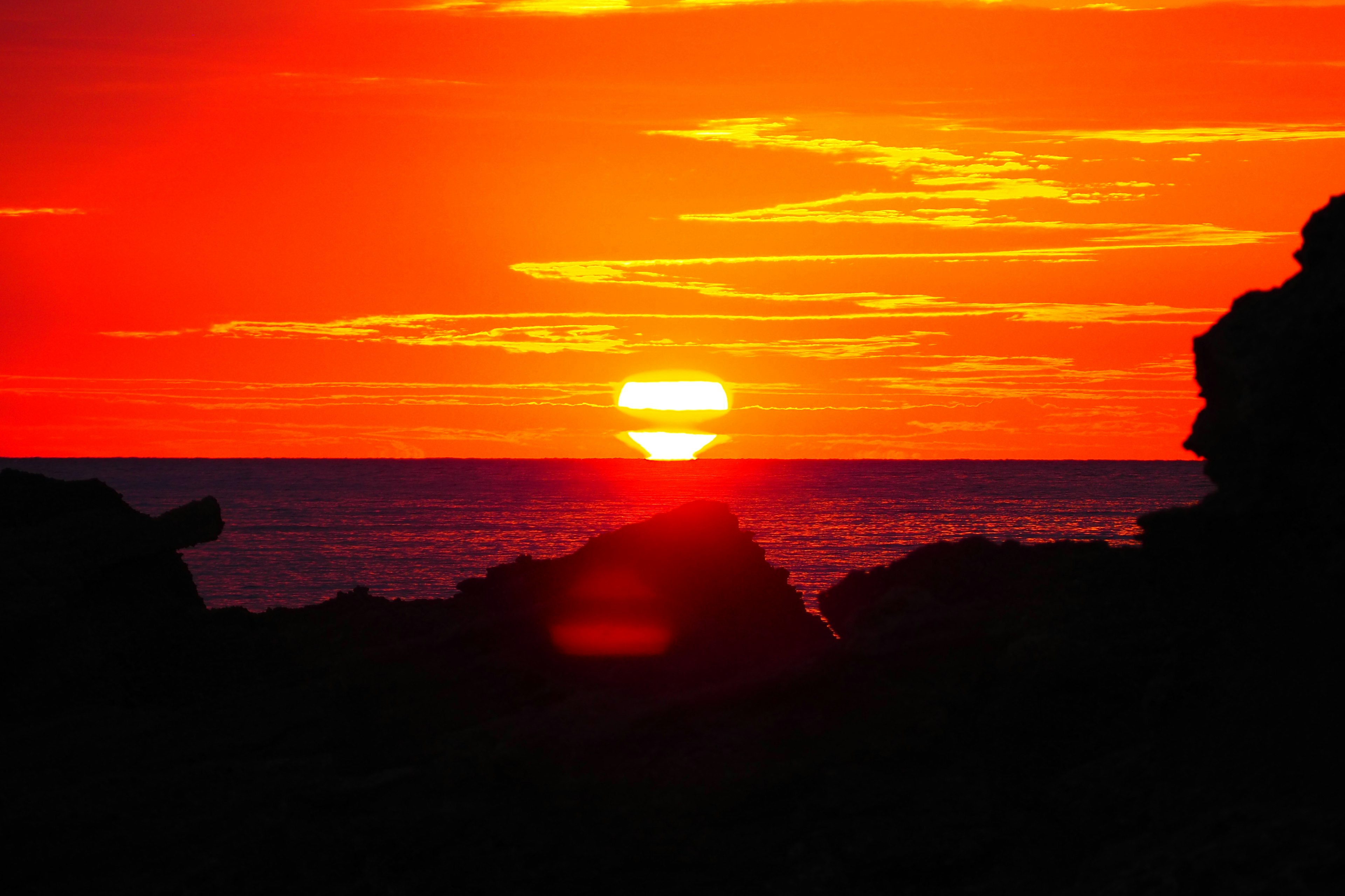 Atardecer naranja sobre el océano con rocas visibles en primer plano