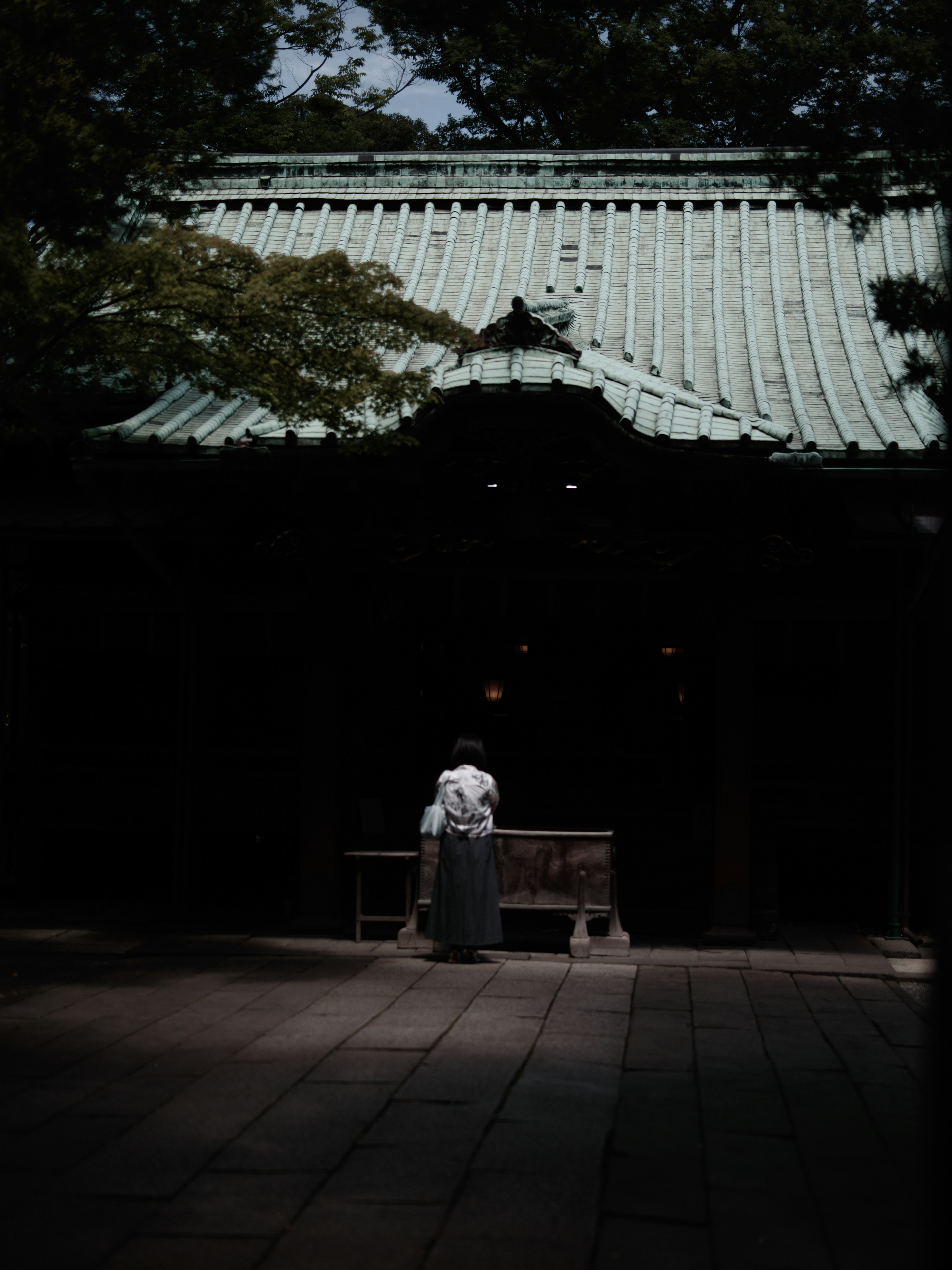 Une personne en kimono blanc se tenant devant un sanctuaire avec un toit vert