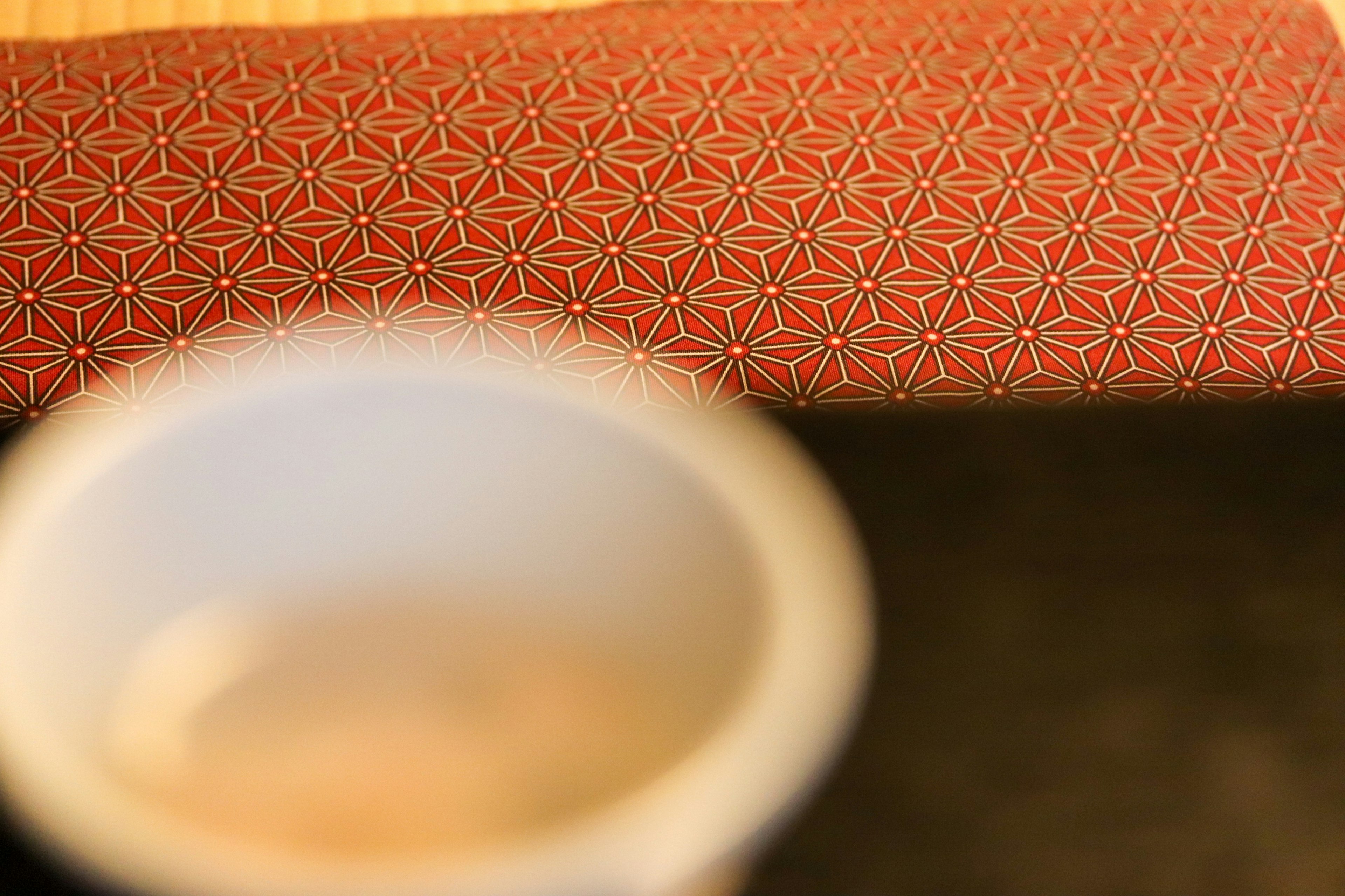 A white tea bowl on a red geometric patterned cloth