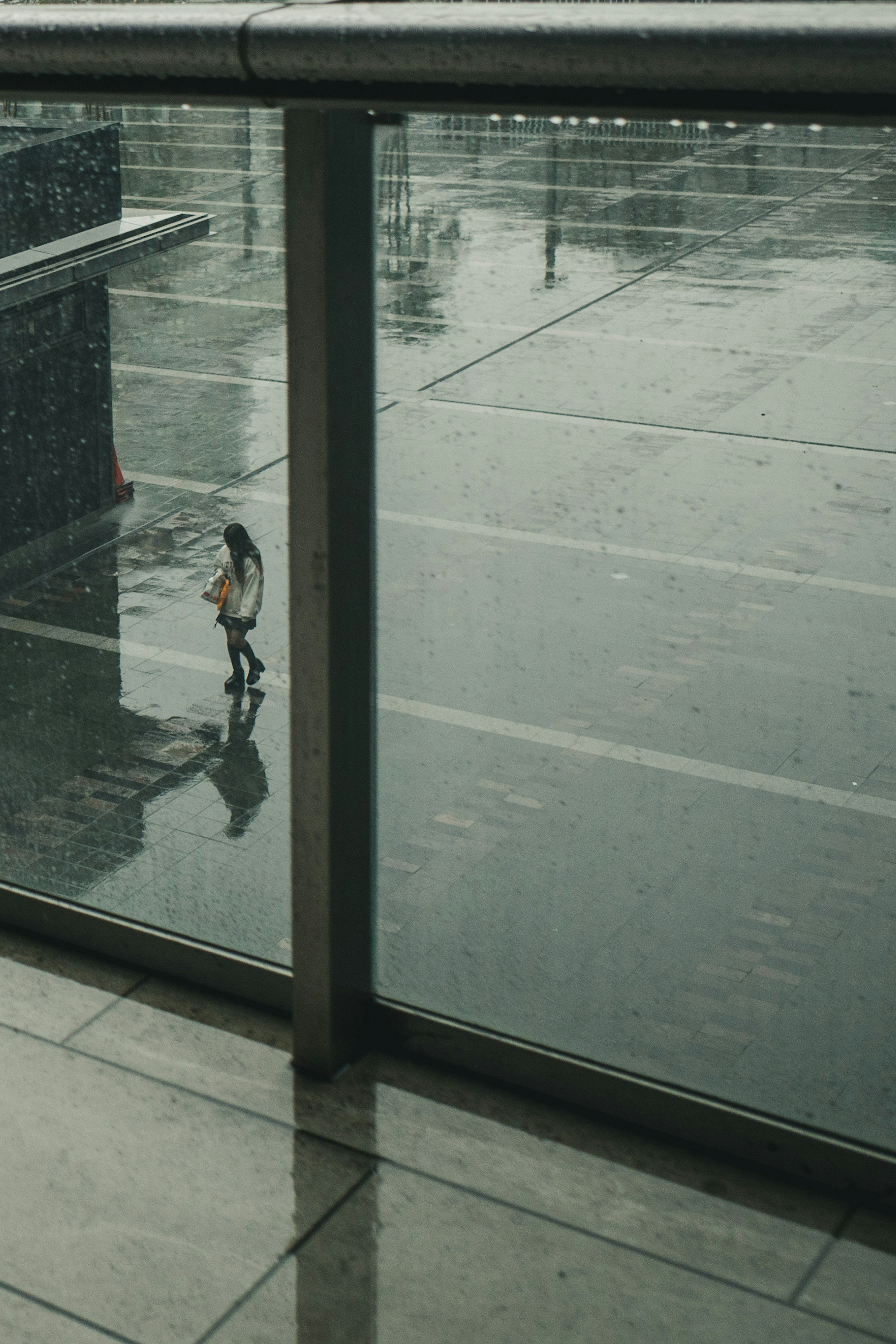 Una mujer caminando bajo la lluvia con una barandilla de vidrio en primer plano