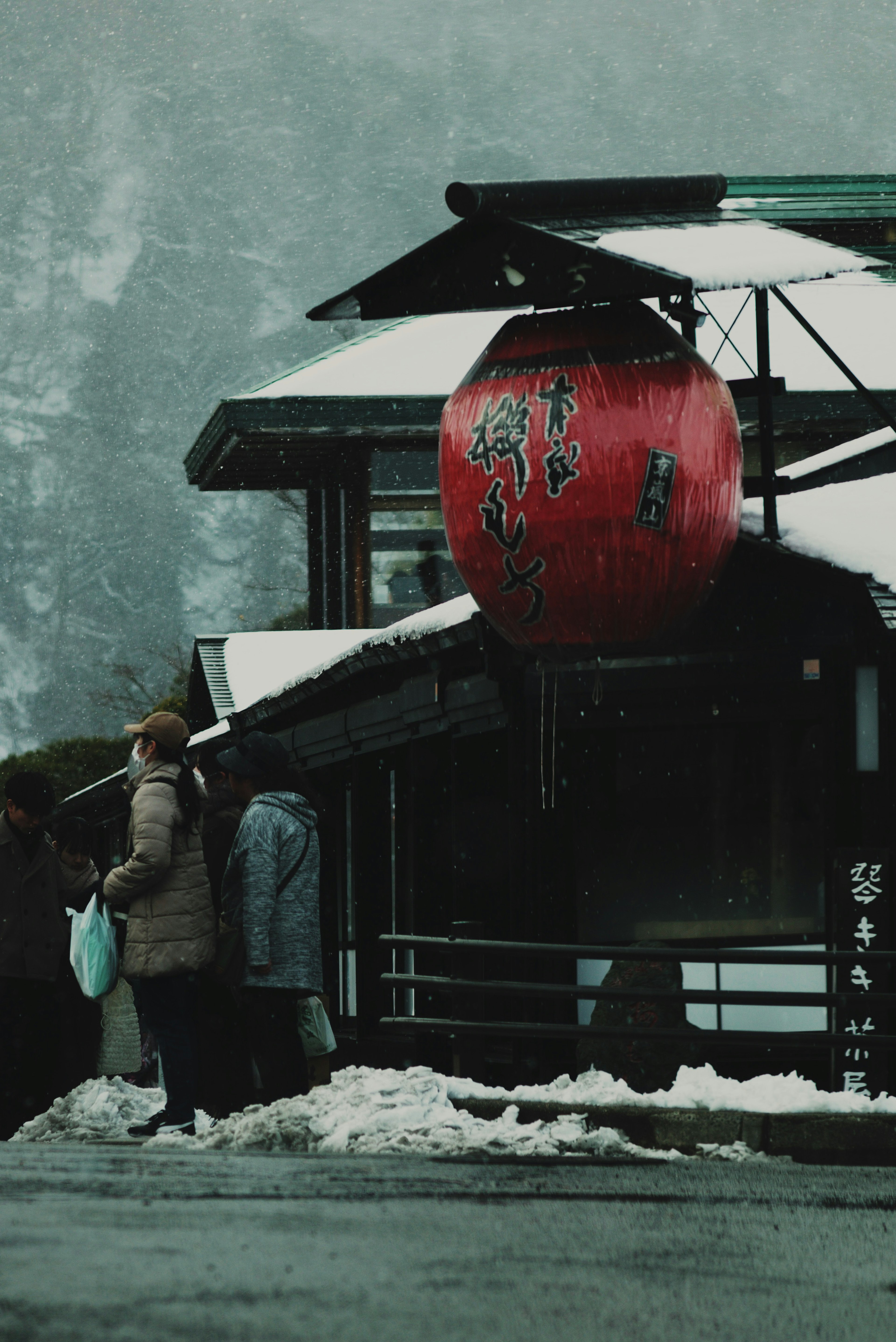 Person steht im Schnee neben einer großen roten Laterne an einem japanischen Gebäude