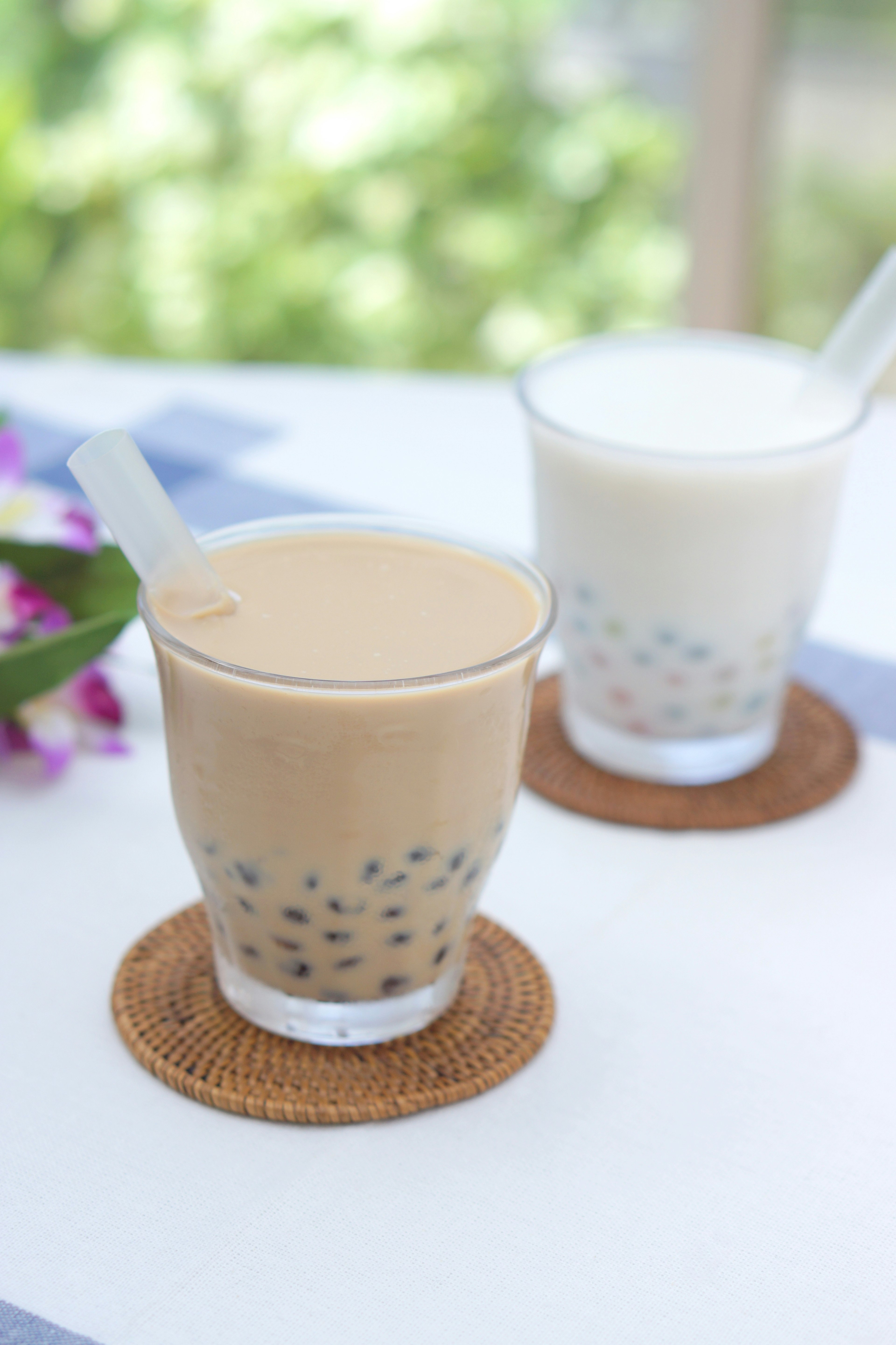 Due bicchieri di tè con perle e latte su un tavolo con sfondo verde sfocato