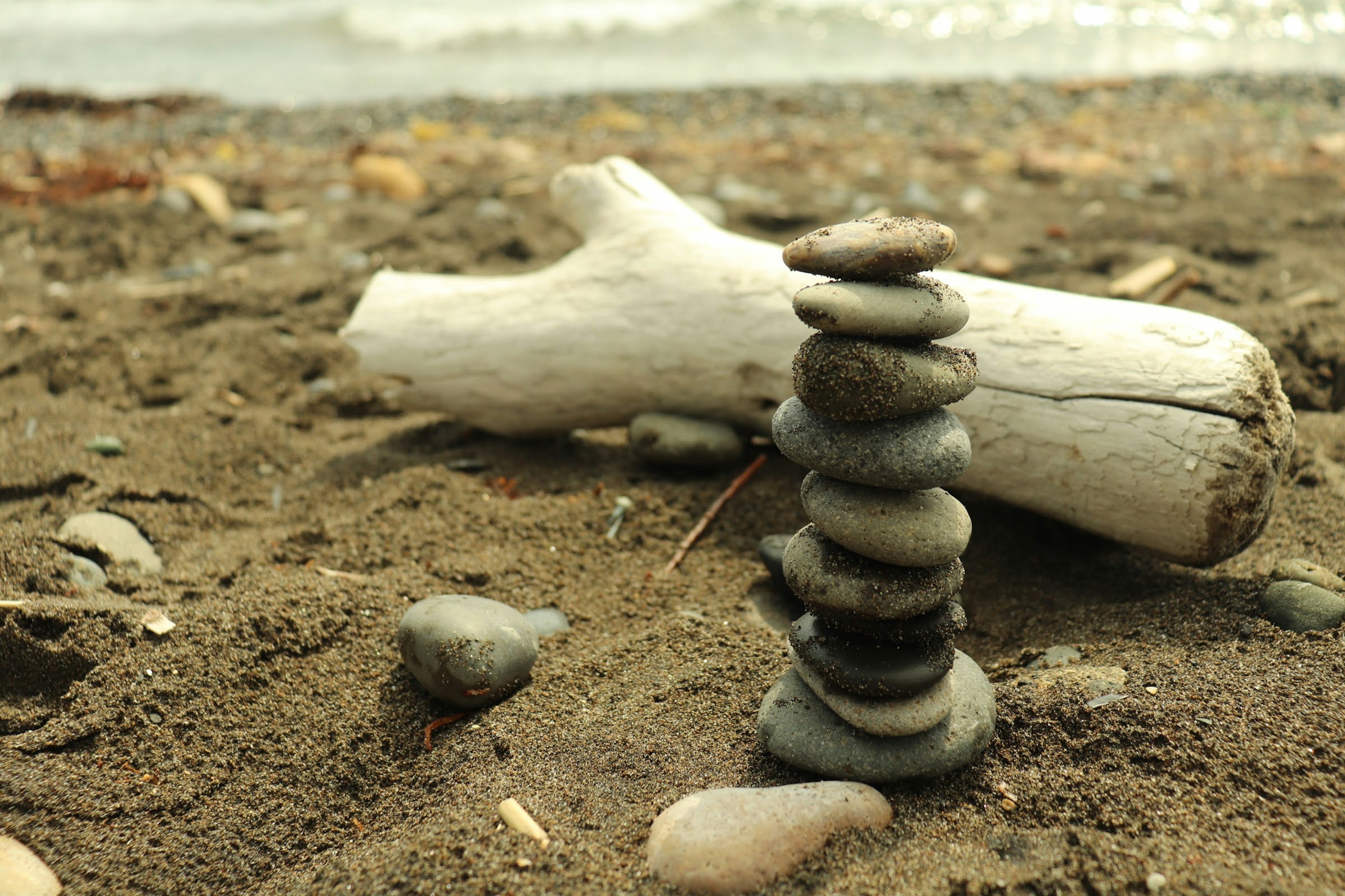 Pila de piedras en una playa de arena con madera flotante