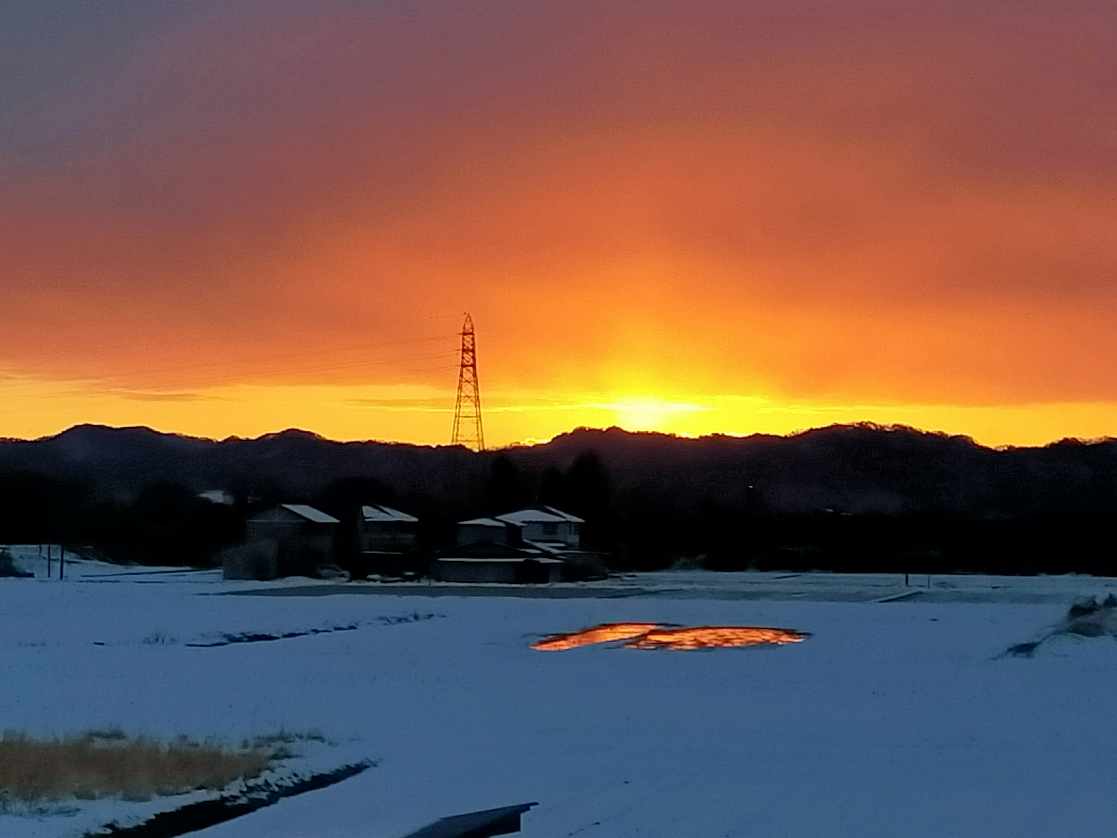 雪に覆われた田んぼと夕日が映る山の風景