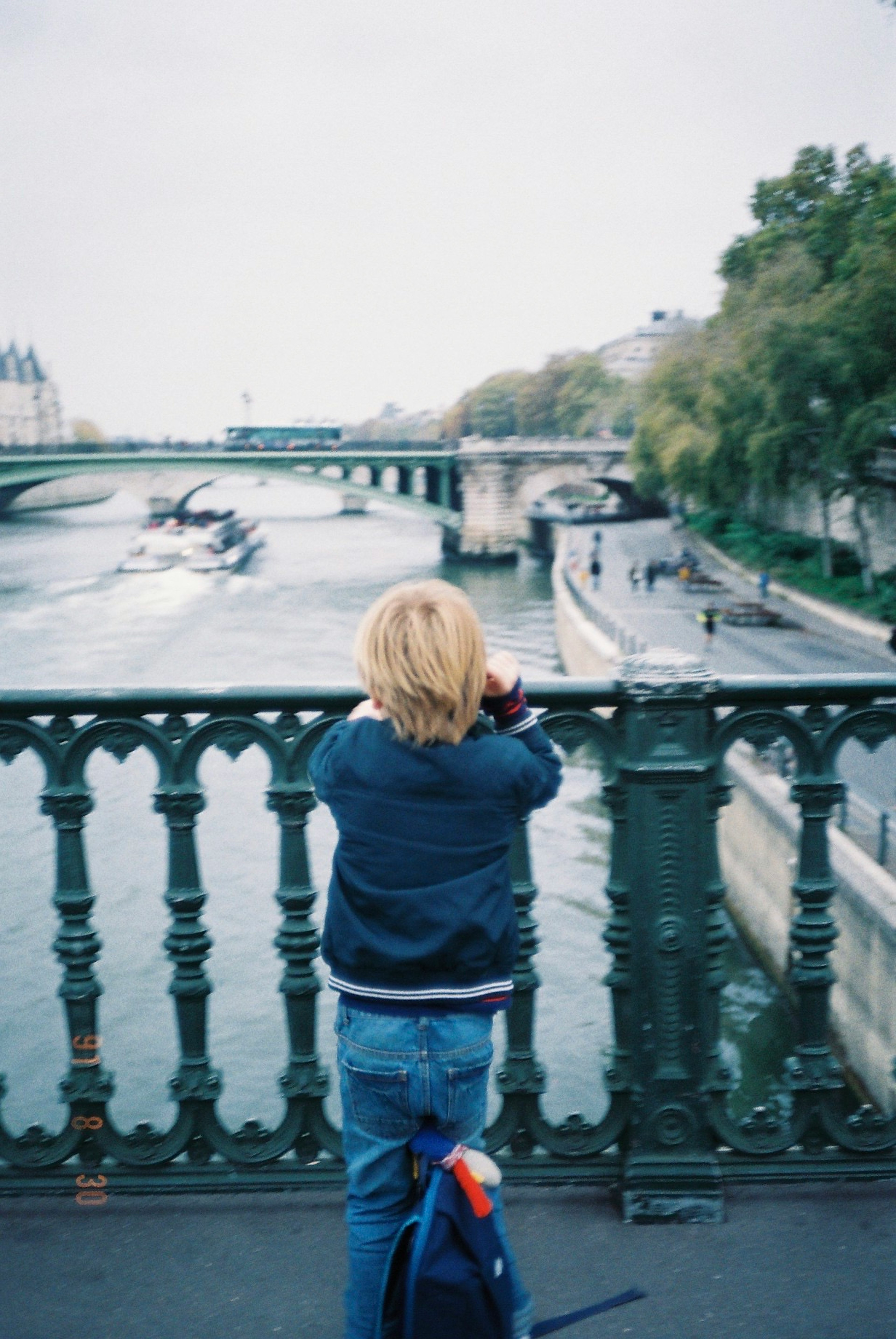 A child standing on a bridge looking at the Seine River