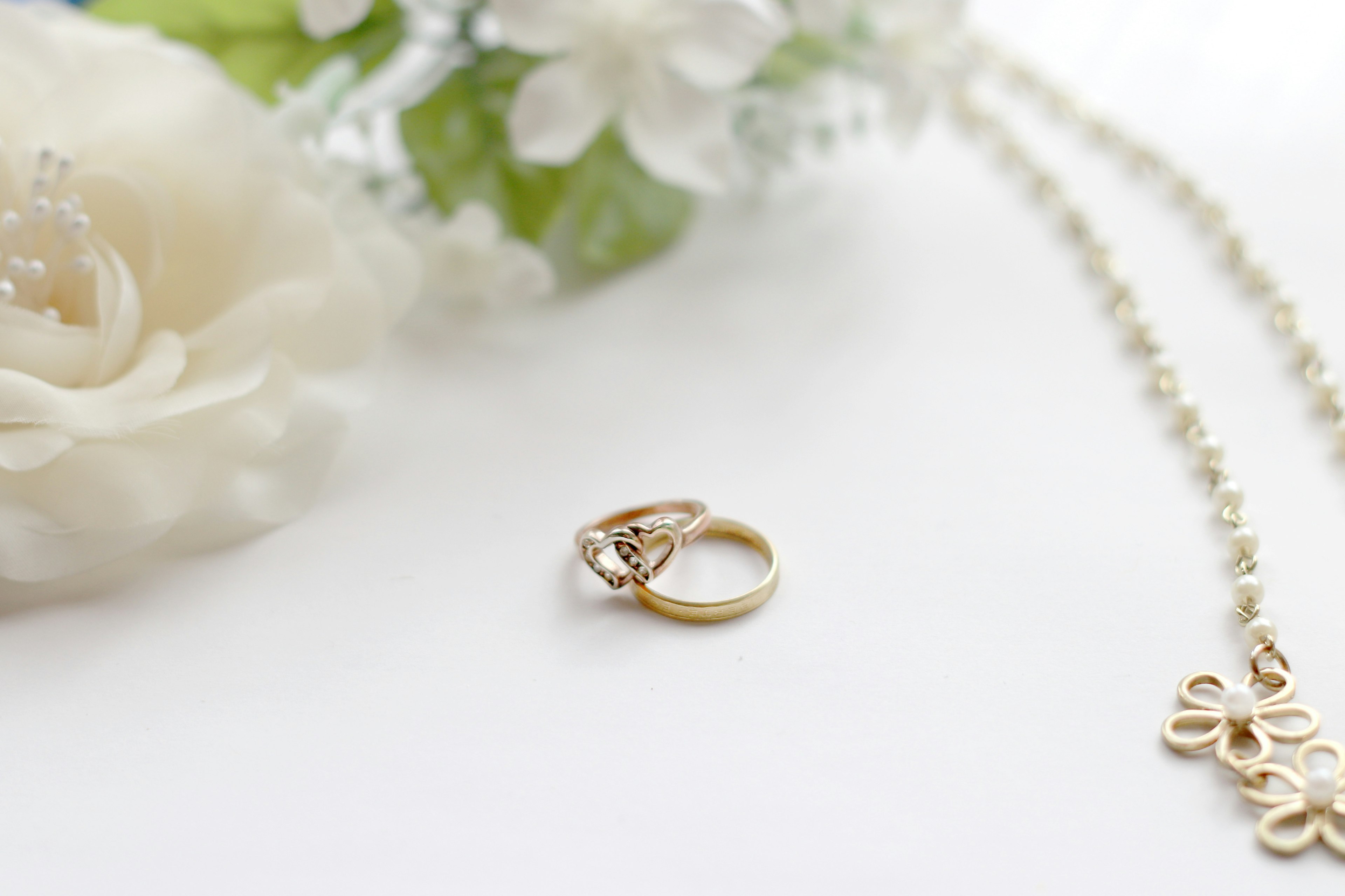 Gold wedding ring and pearl necklace placed on a white background