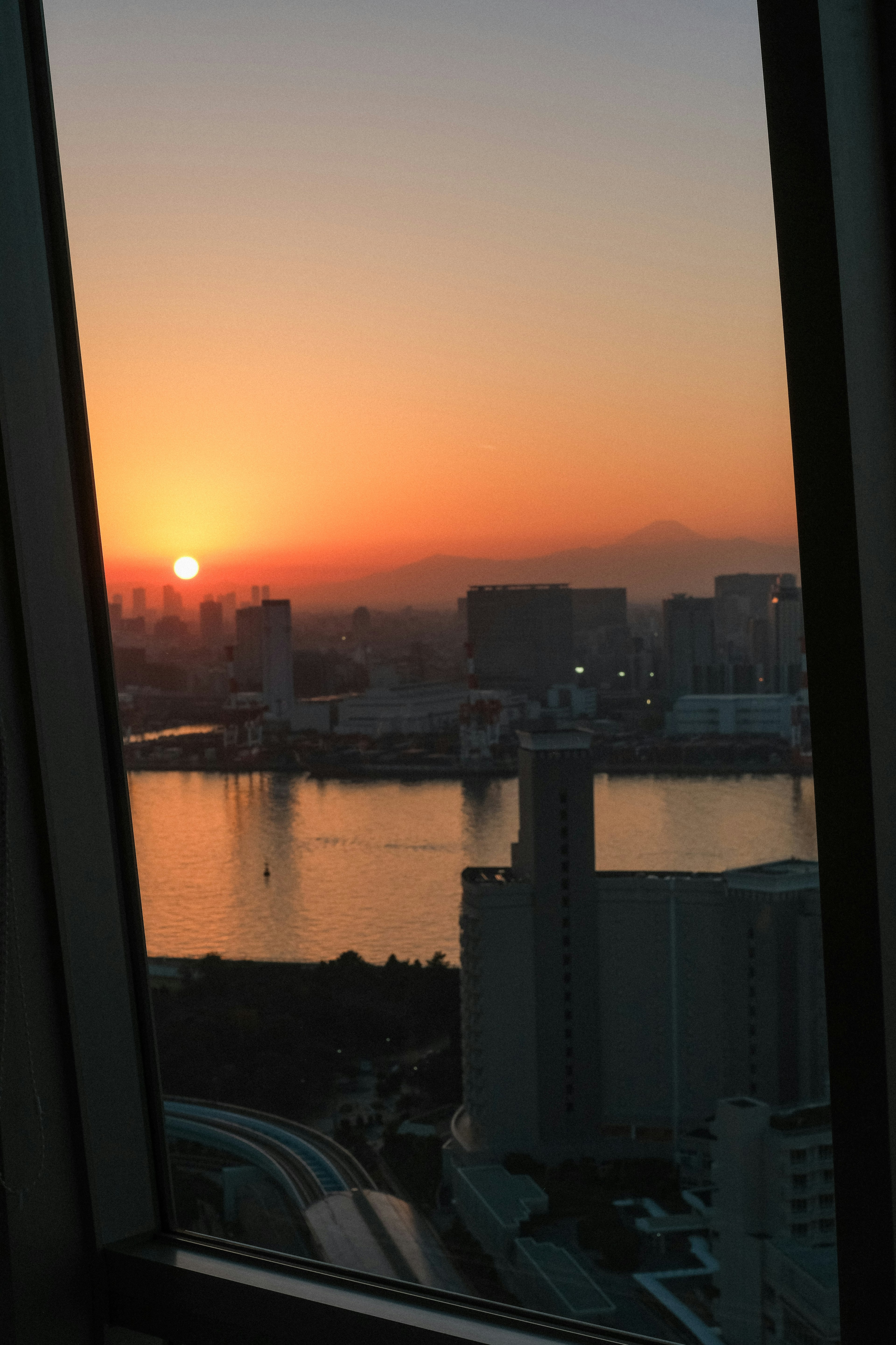 Stadtansicht bei Sonnenuntergang durch ein Fenster mit orangefarbenem Himmel auf dem Wasser