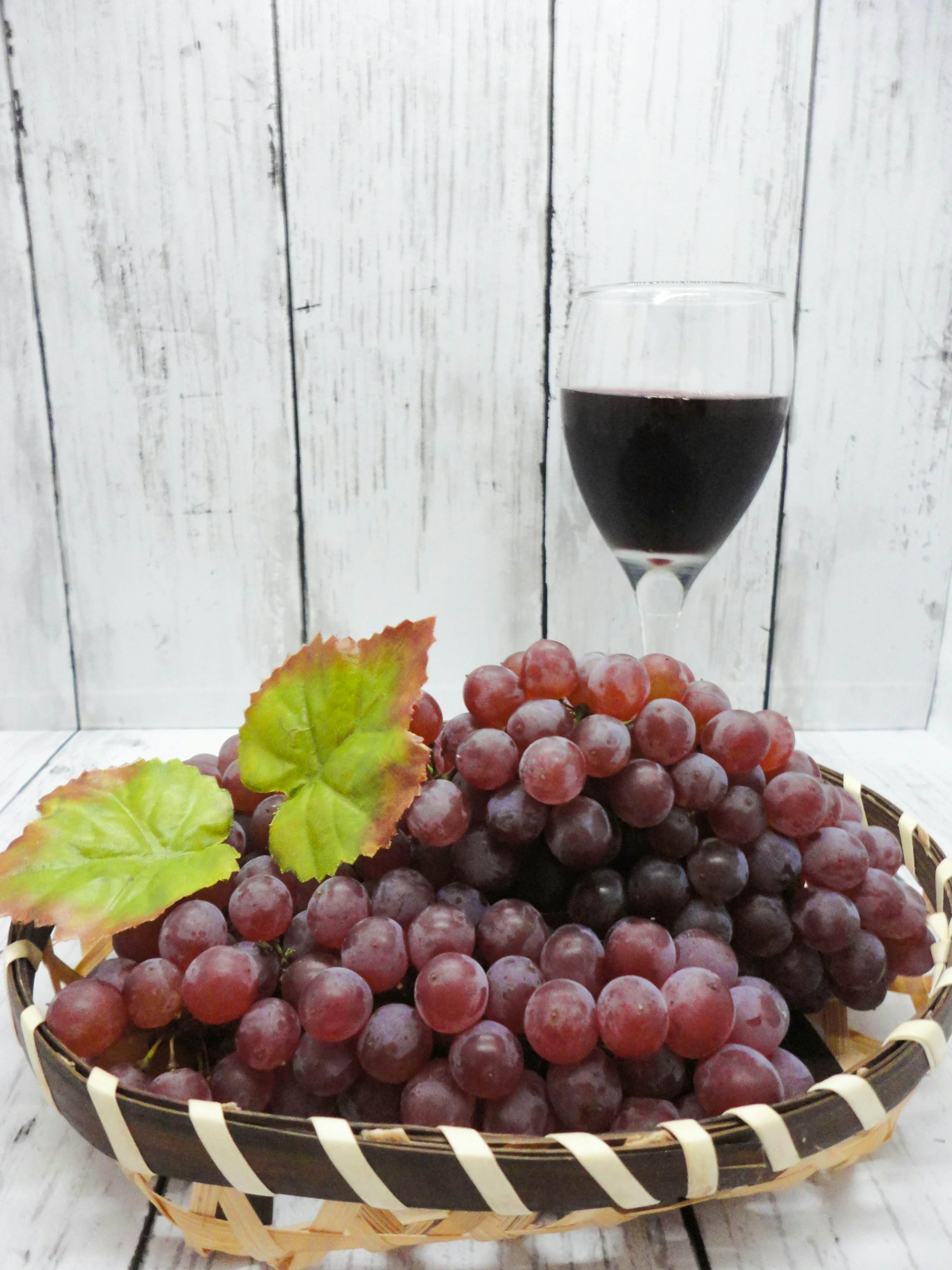 A bunch of red grapes with a glass of red wine on a wooden table