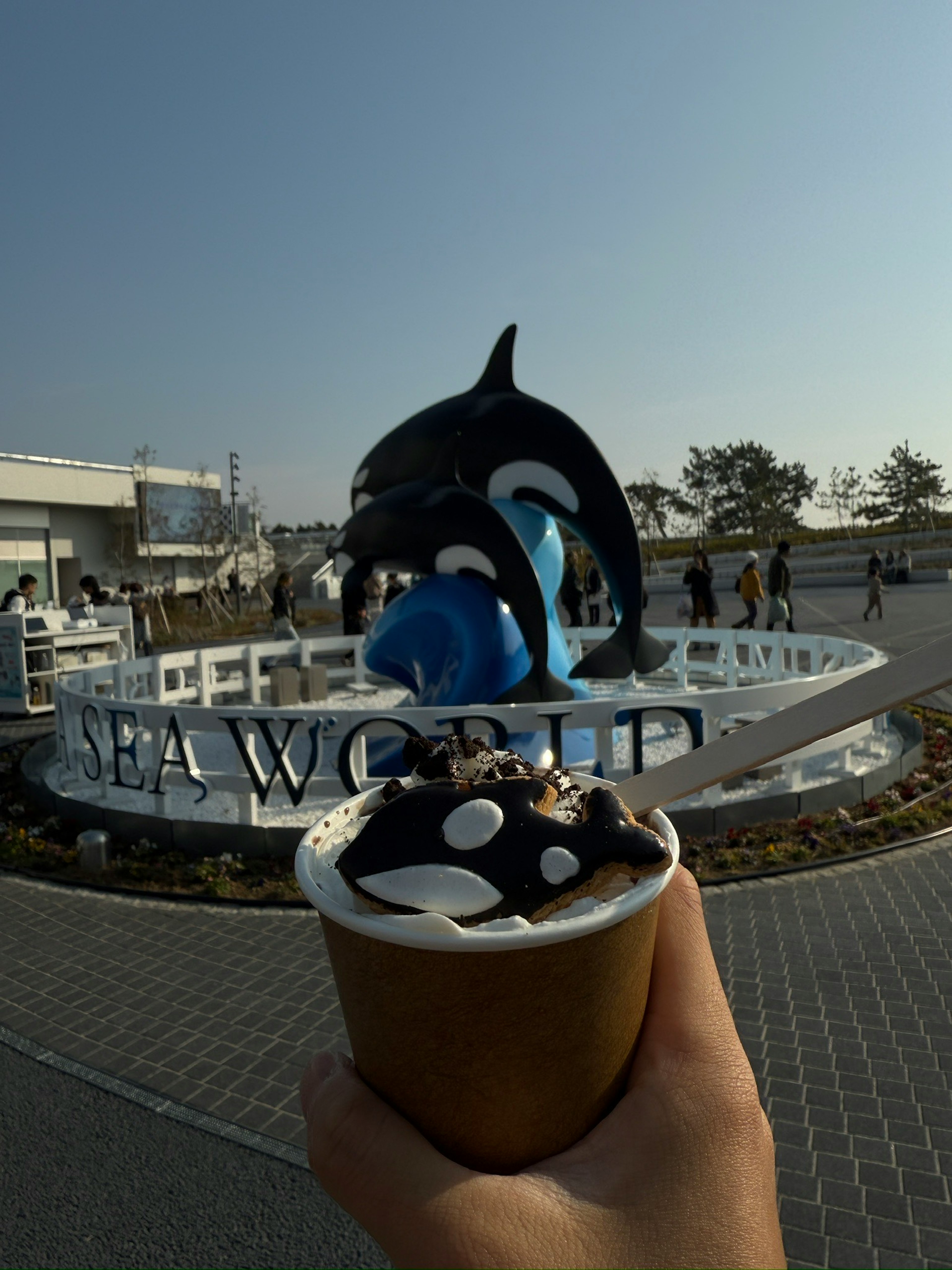 Une main tenant une glace devant un panneau SeaWorld et une statue d'orque